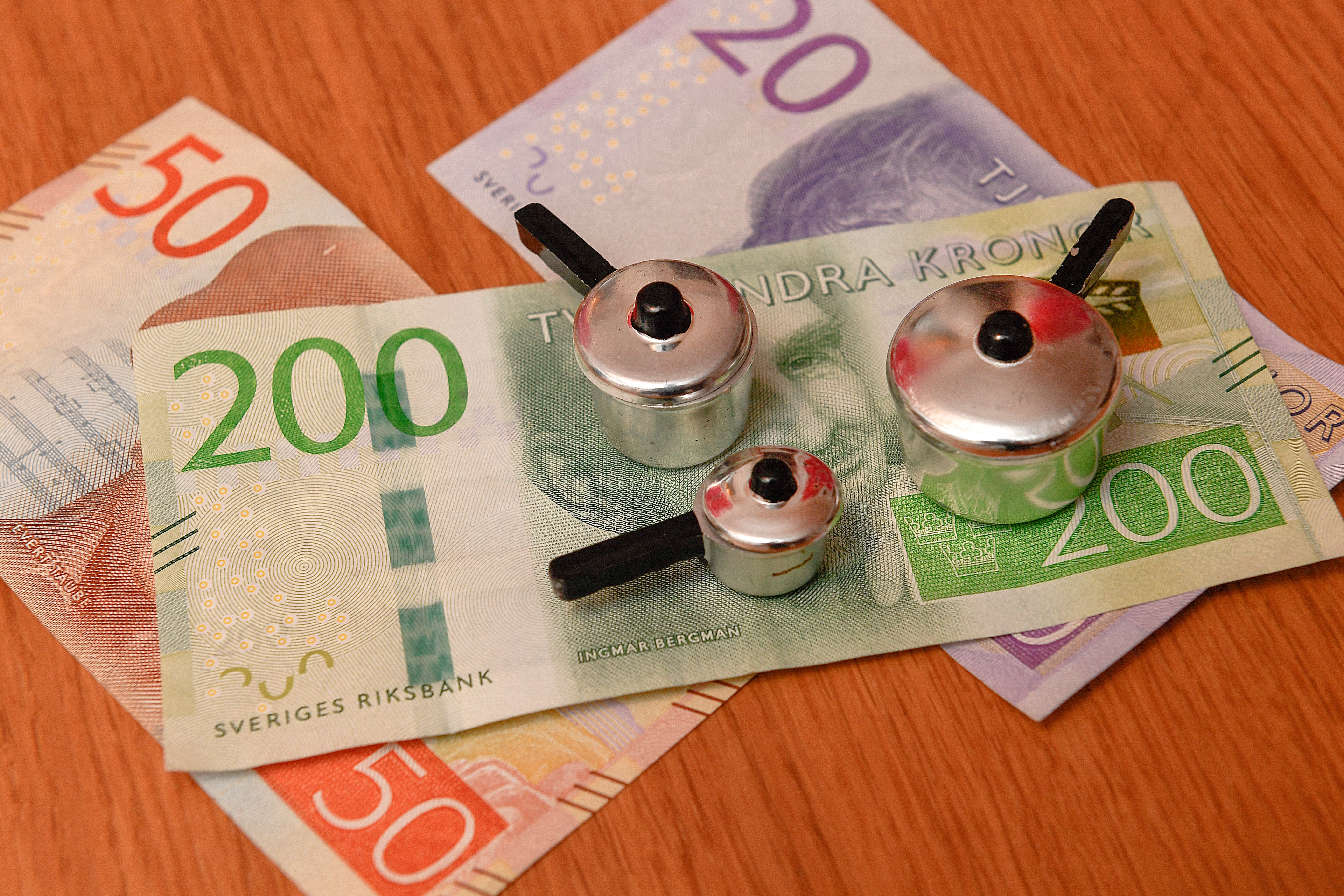 Svenska sedlar av olika valörer tillsammans med tre små metalliska leksaksögon på en träyta.