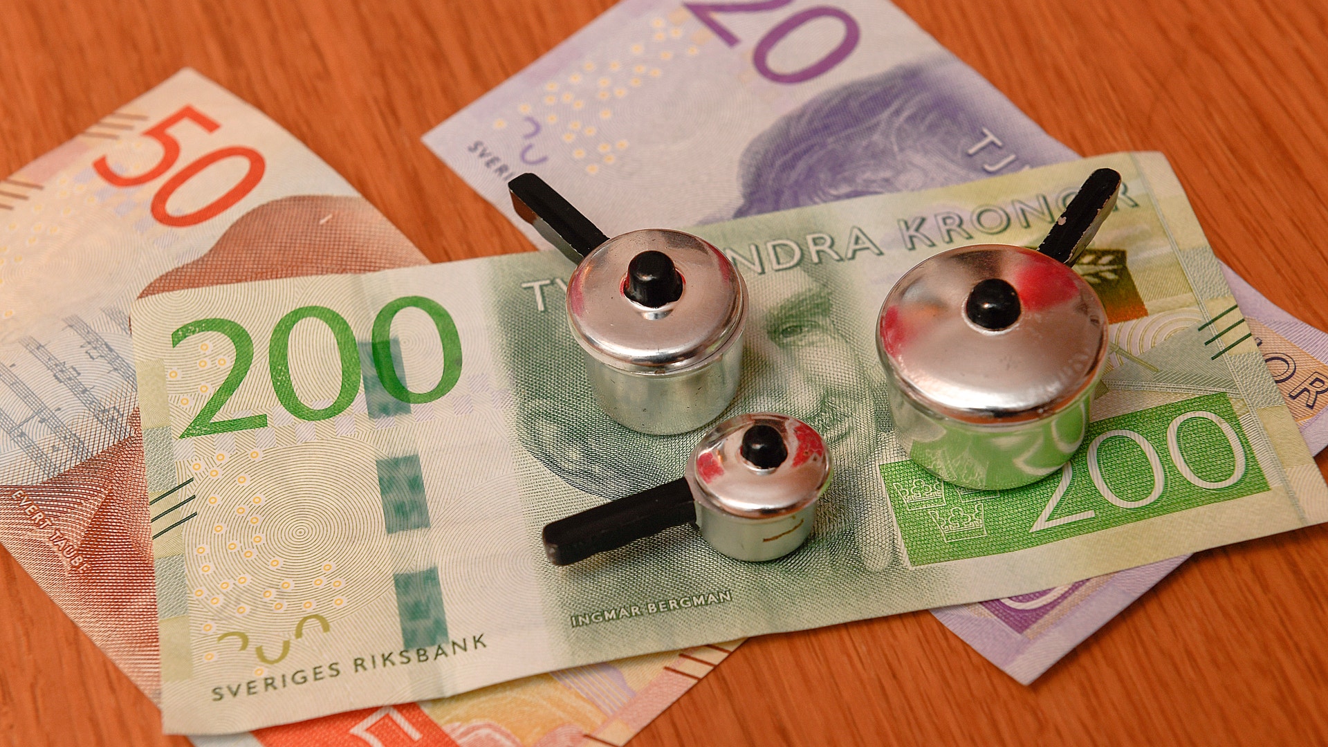 Svenska sedlar av olika valörer tillsammans med tre små metalliska leksaksögon på en träyta.