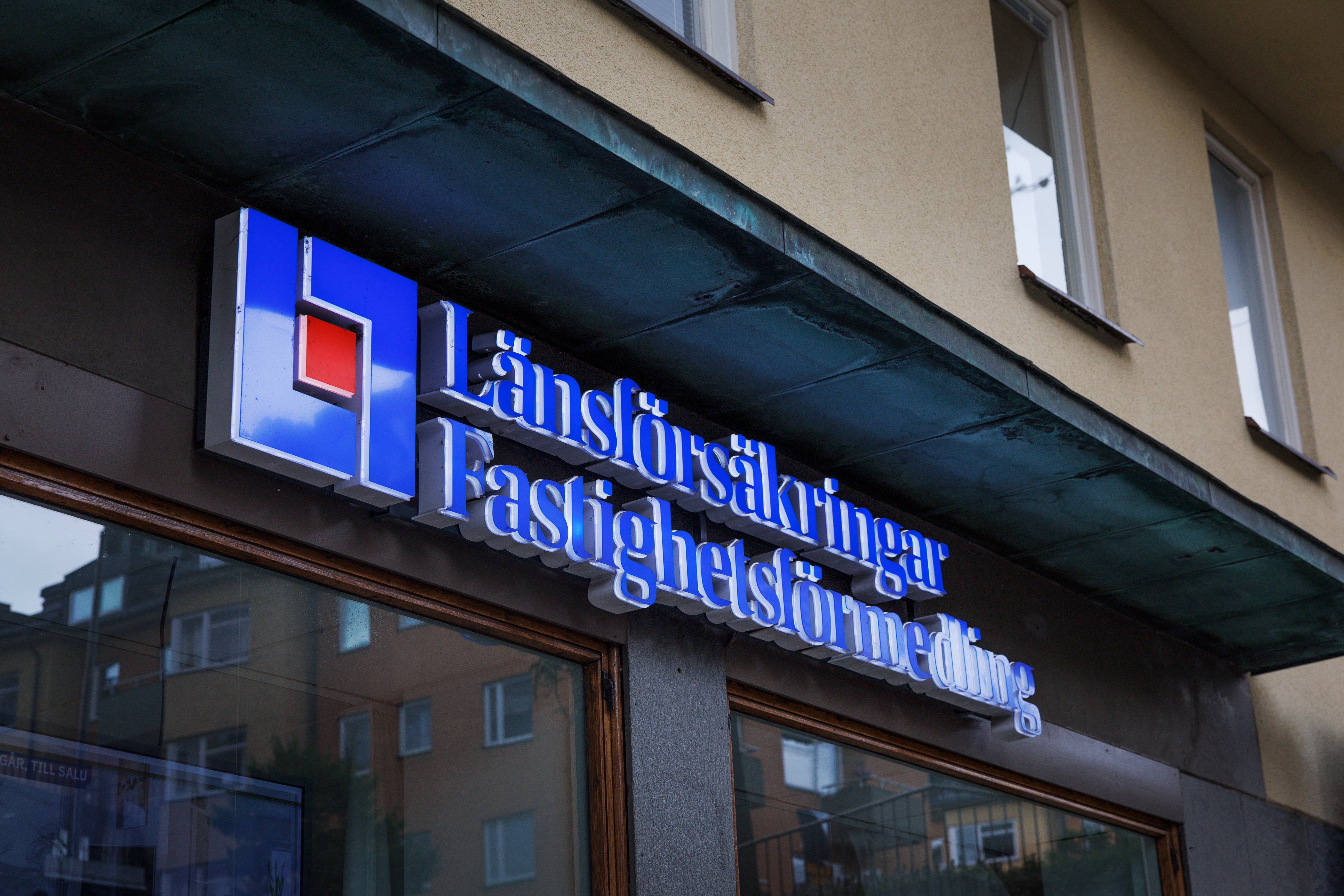 Blå upplysta skyltar med texten "Länsförsäkringar Fastighetsförmedling" på en husfasad.