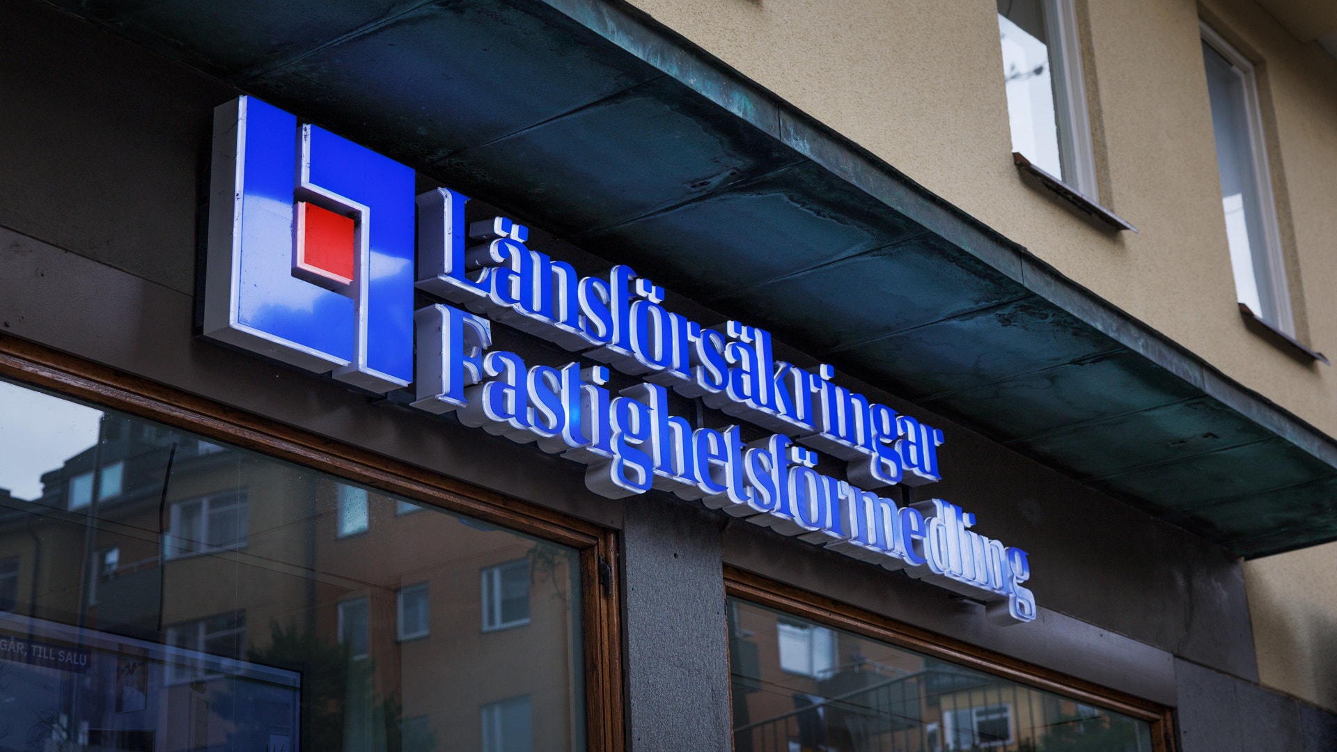Blå upplysta skyltar med texten "Länsförsäkringar Fastighetsförmedling" på en husfasad.