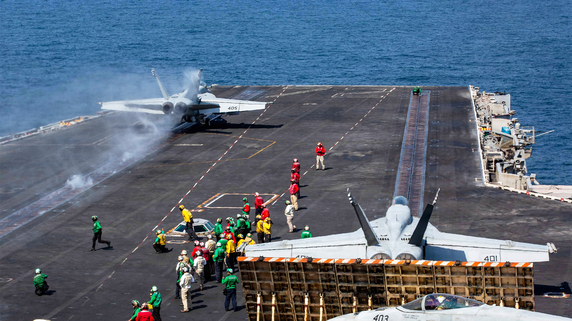 Flygdäck på ett militärt hangarfartyg med personal och stridsflygplan