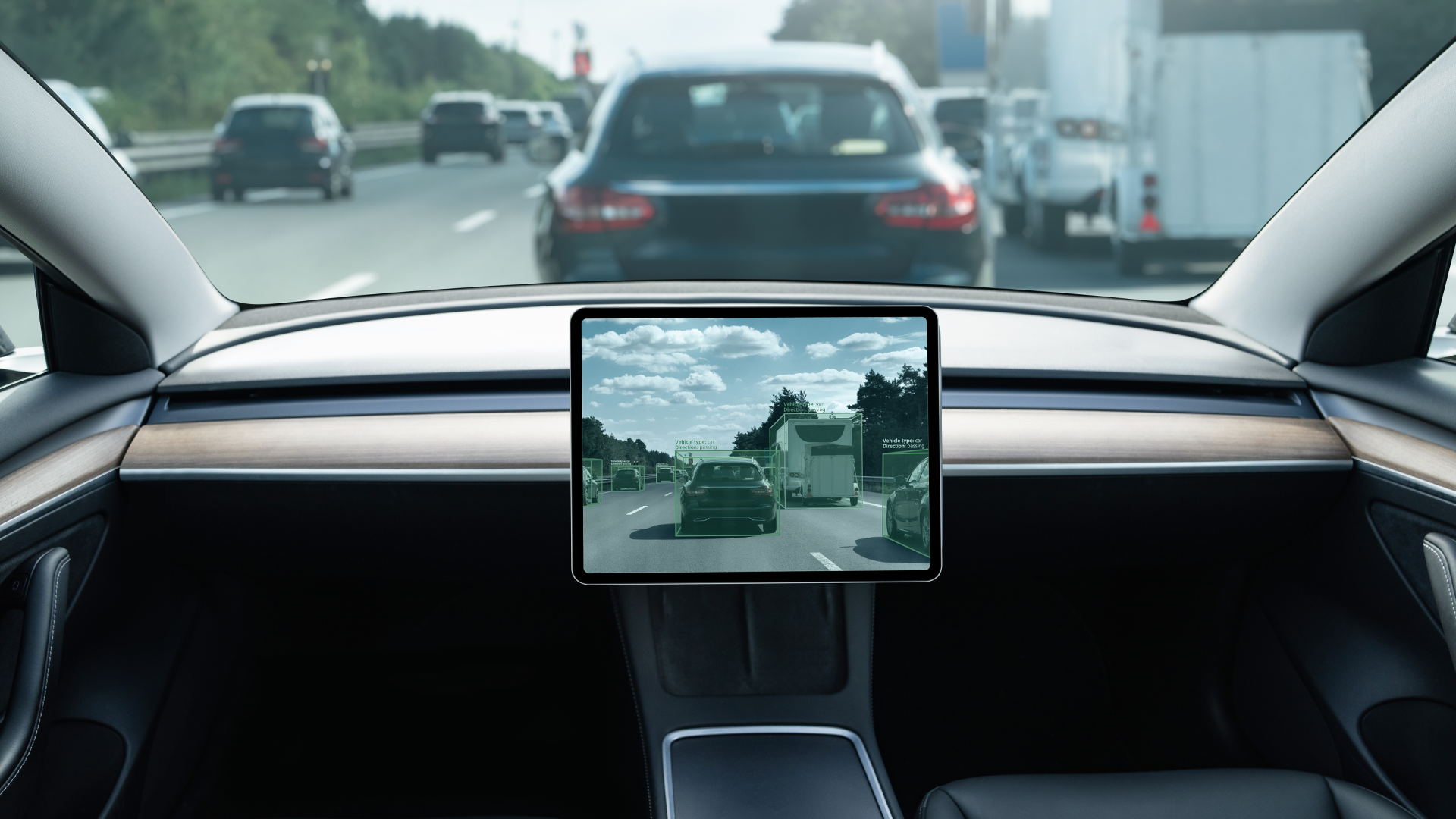 Vy från insidan av en bil på en motorväg. Instrumentpanelen med en stor central skärm syns i förgrunden, och genom vindrutan ses flera fordon på vägen framför.