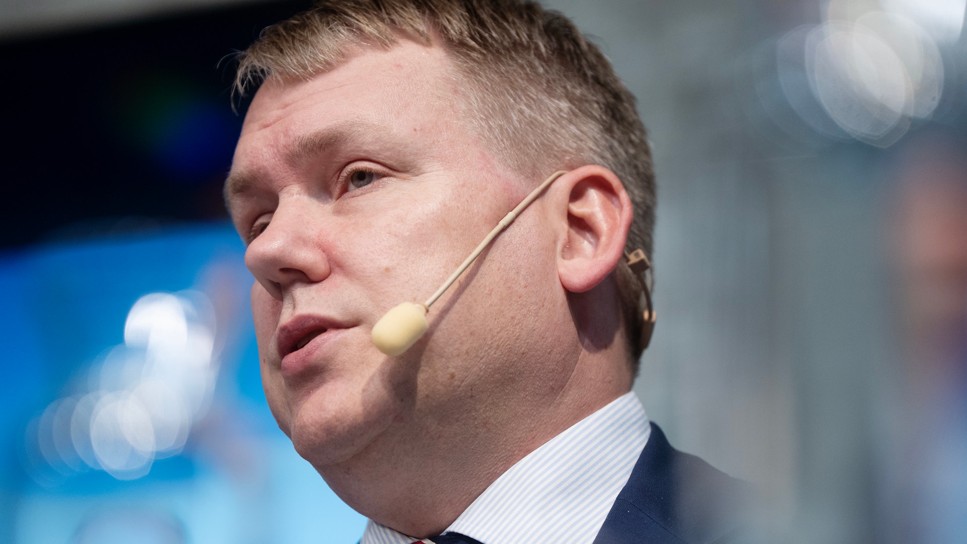 Närbild på en man i kostym och randig slips som talar i en headsetmikrofon.