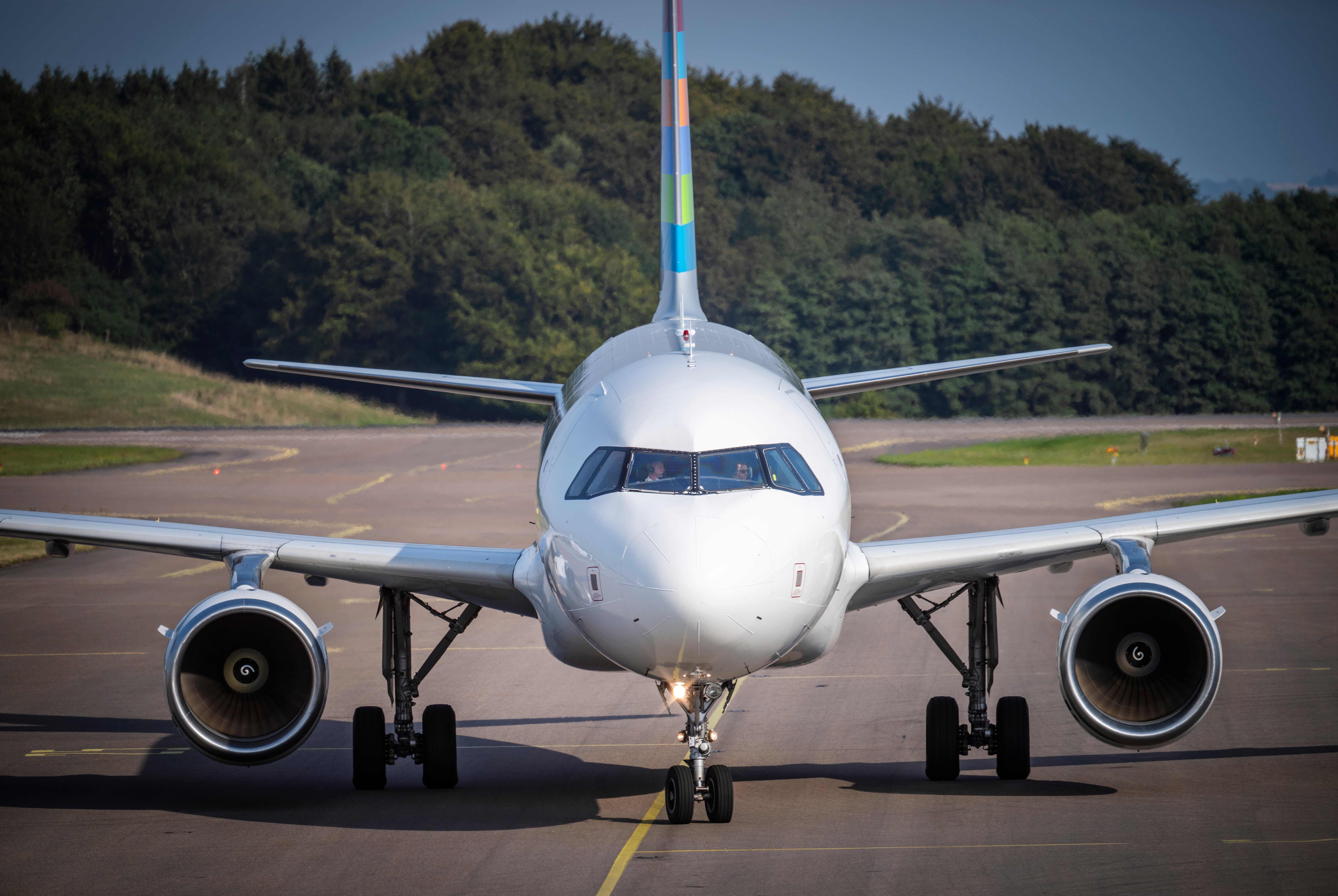 Vitt passagerarflygplan fotograferat framifrån på en flygplats, med två motorer synliga och skogar i bakgrunden.