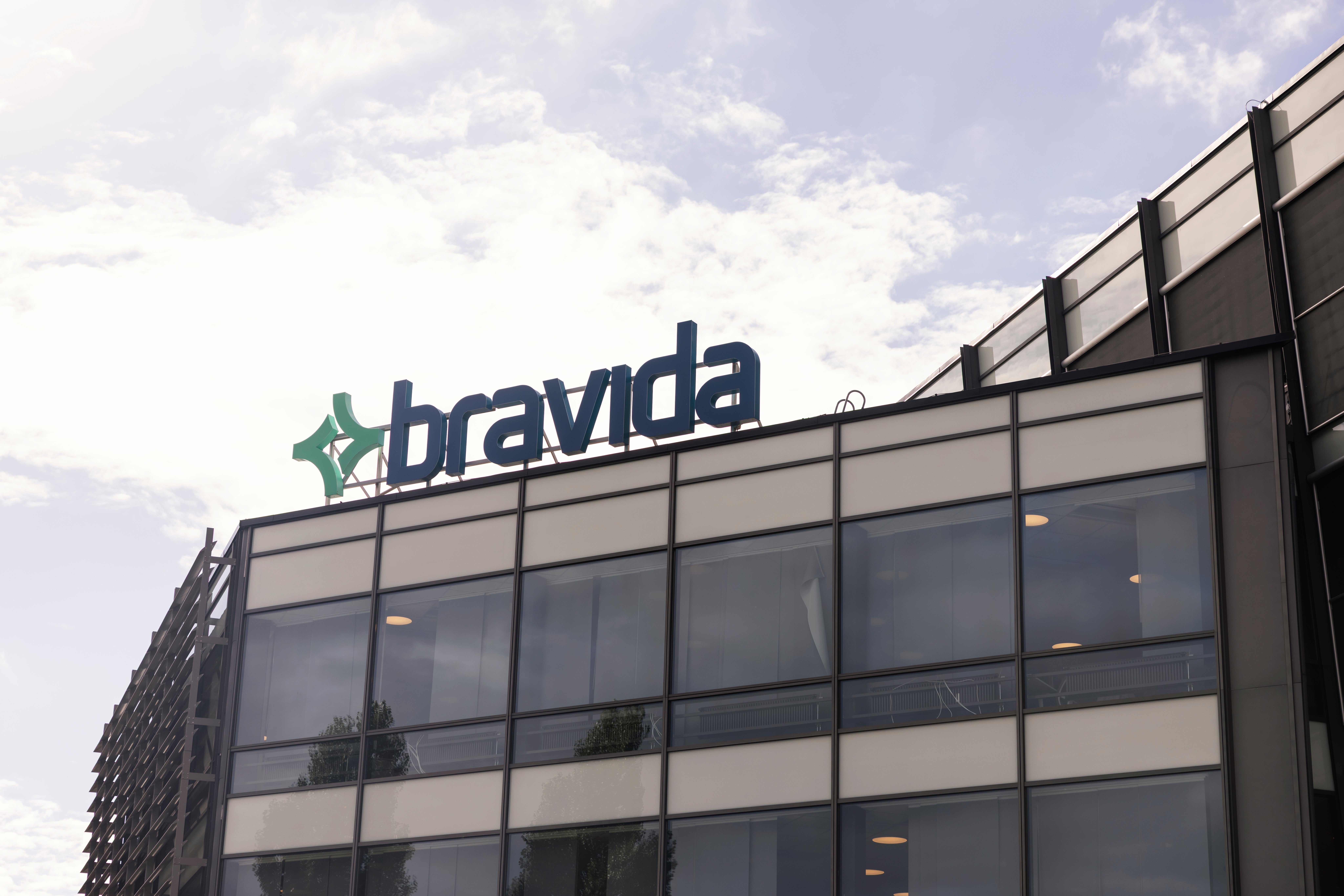 Kontorsbyggnad med Bravida-logotypen på taket. Modern fasad med glas och betong mot molnig himmel.