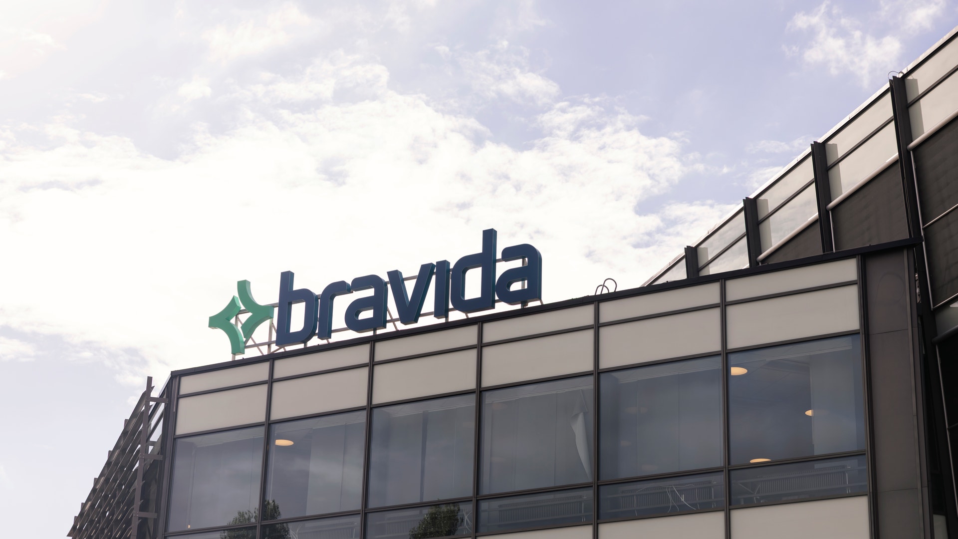 Kontorsbyggnad med Bravida-logotypen på taket. Modern fasad med glas och betong mot molnig himmel.