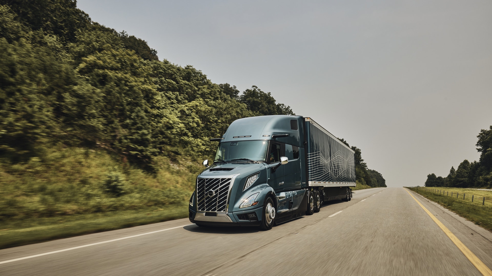 En modern lastbil kör på en motorväg omgiven av grön vegetation.