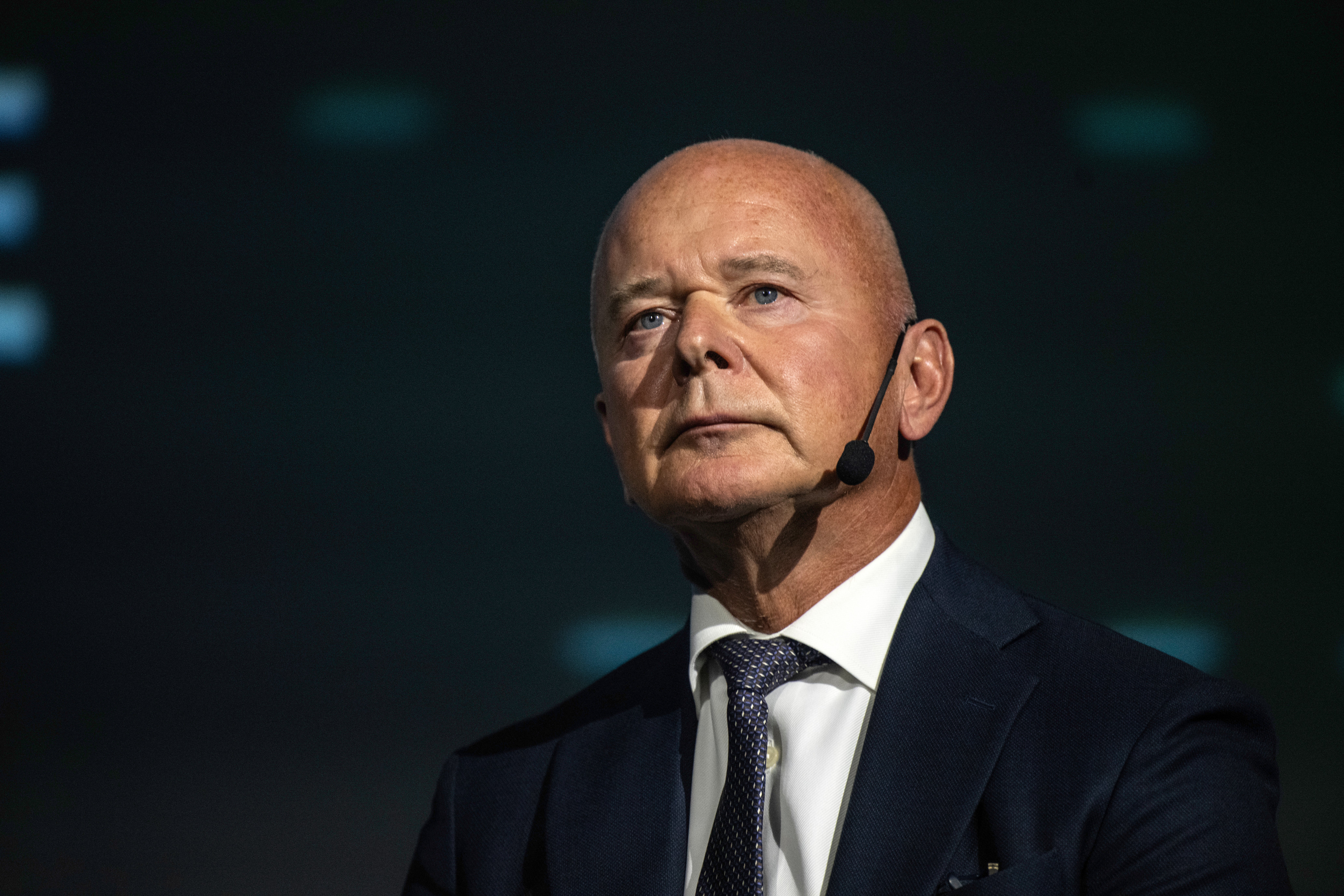 Porträtt av en man i mörk kostym och slips mot mörk bakgrund.