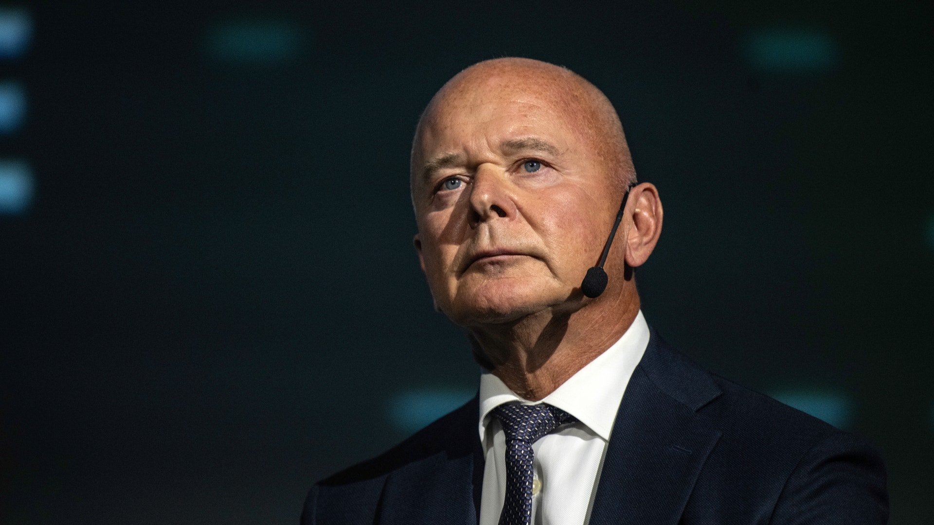 Porträtt av en man i mörk kostym och slips mot mörk bakgrund.