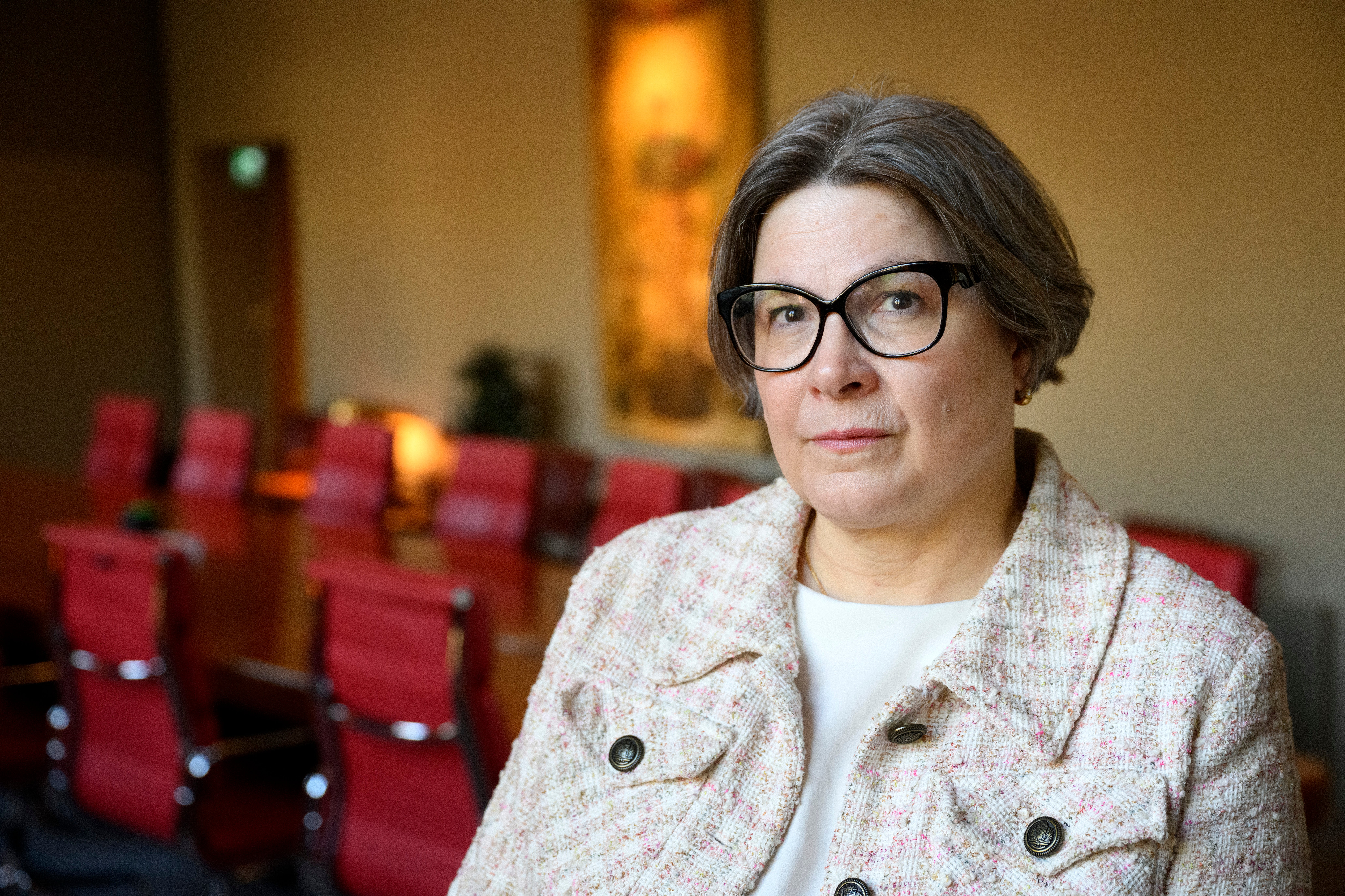 Kvinna med glasögon sitter i en auditorium med röda stolar i bakgrunden.