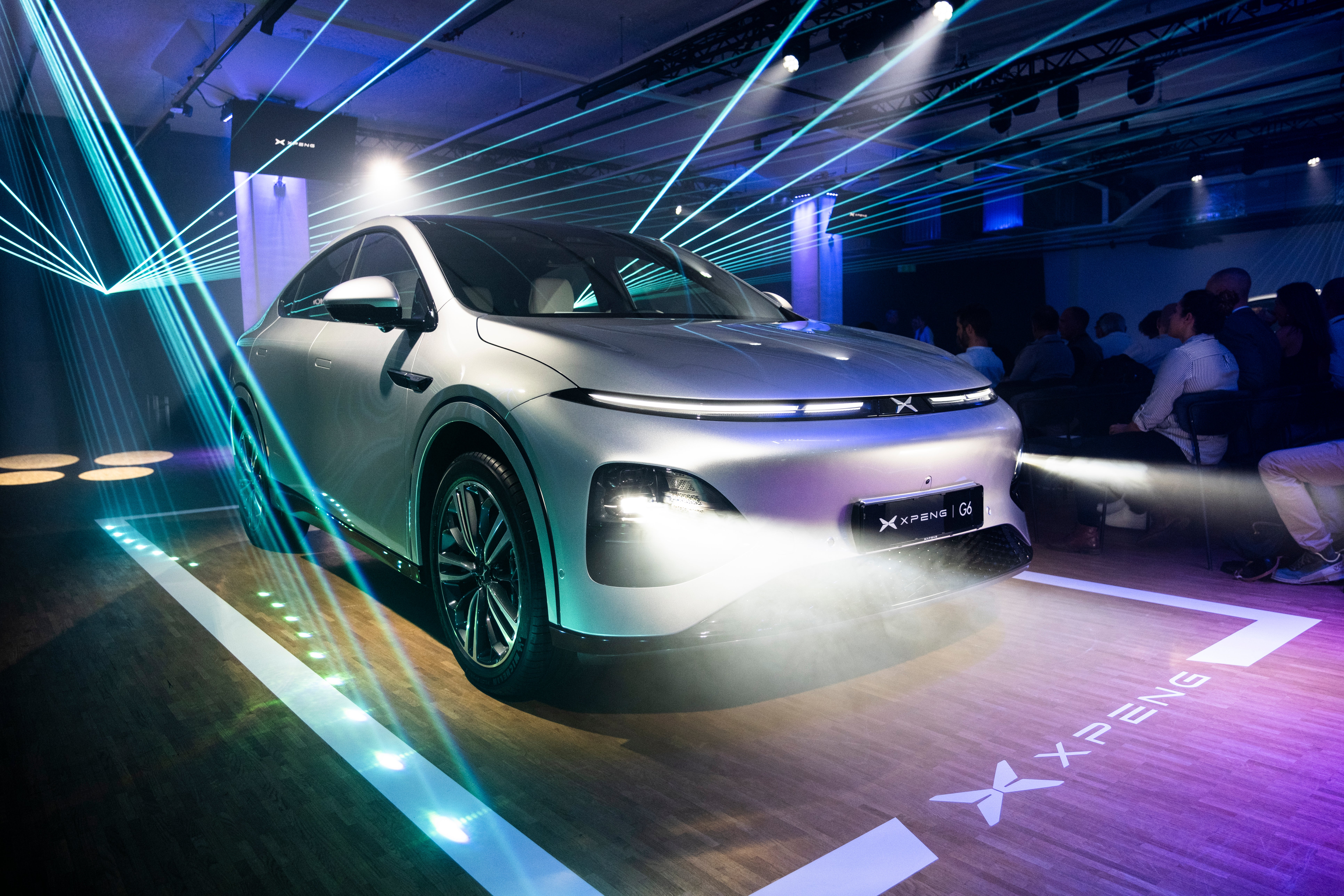 En vit elektrisk bil utställd i ett futuristiskt utställningsrum med blå och lila neonljus.