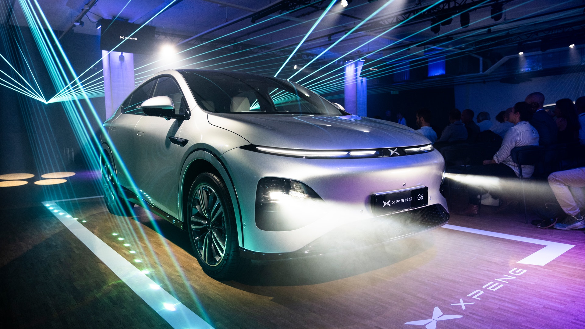 En vit elektrisk bil utställd i ett futuristiskt utställningsrum med blå och lila neonljus.