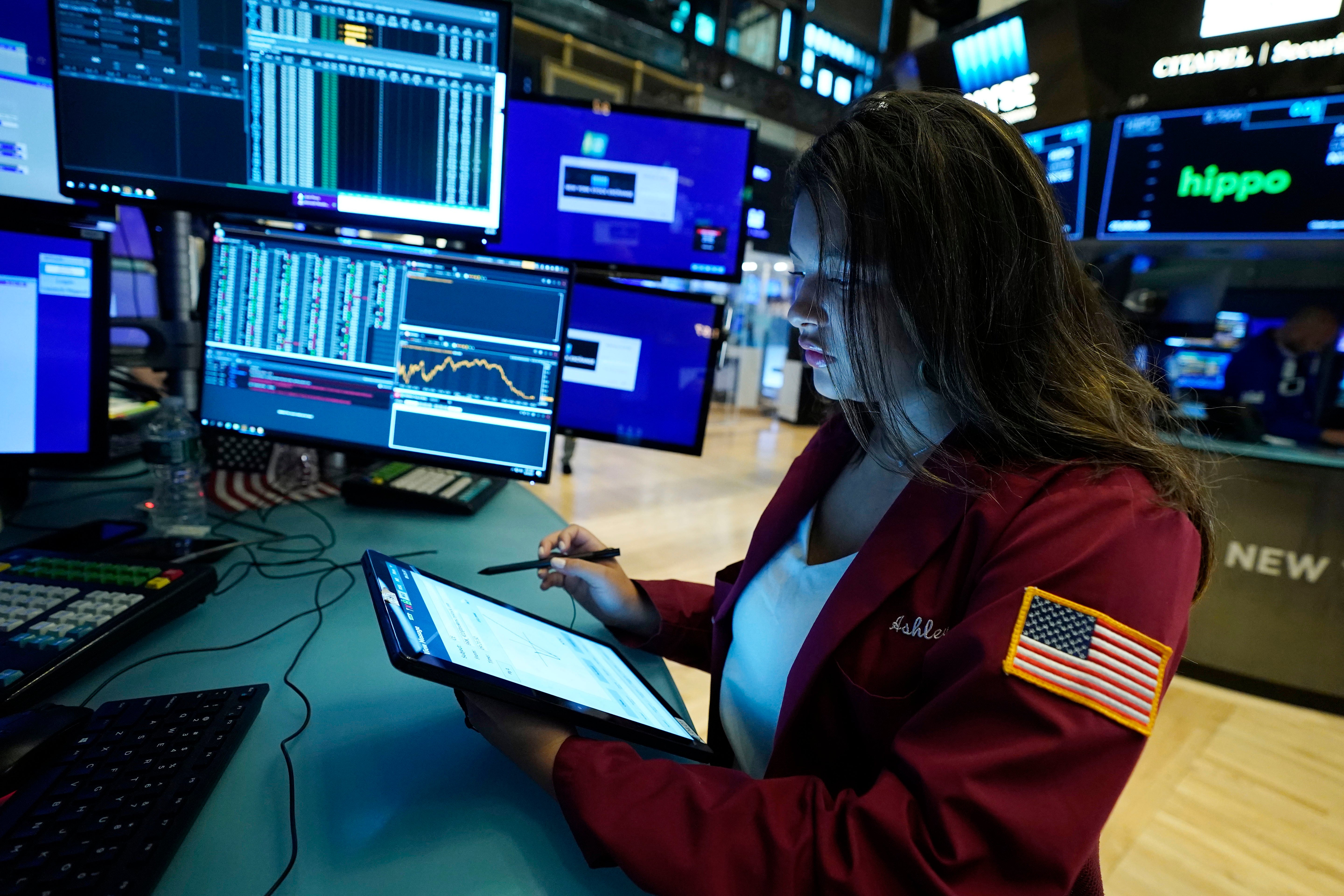 En person i röd jacka arbetar vid en datorstation med flera skärmar som visar finansiell data och diagram.