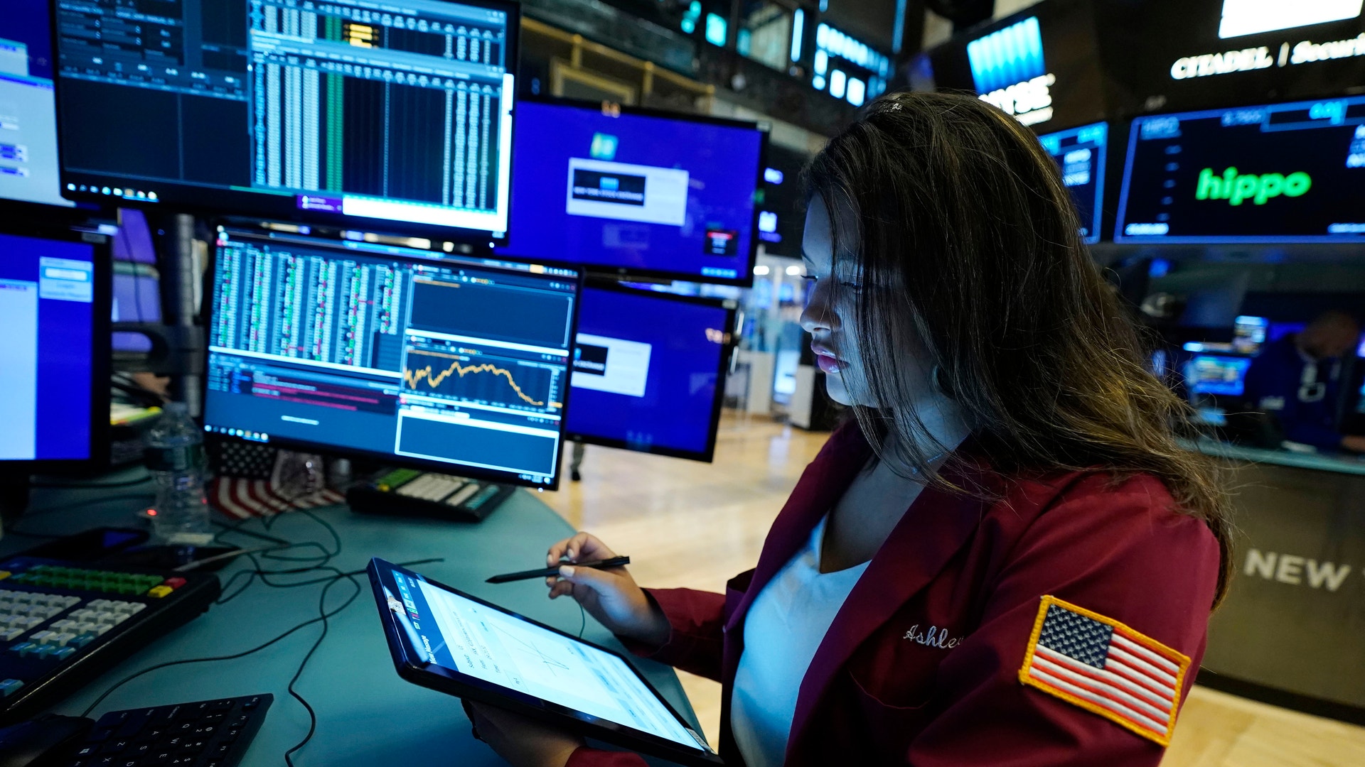 En person i röd jacka arbetar vid en datorstation med flera skärmar som visar finansiell data och diagram.