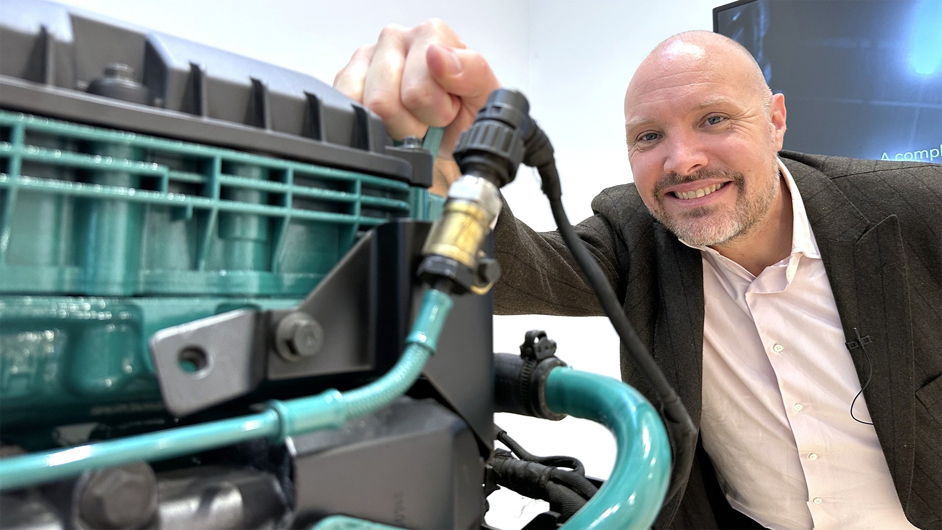 Man i kostym håller upp en laddkontakt framför en elektrisk Volvo-bil och ler mot kameran.