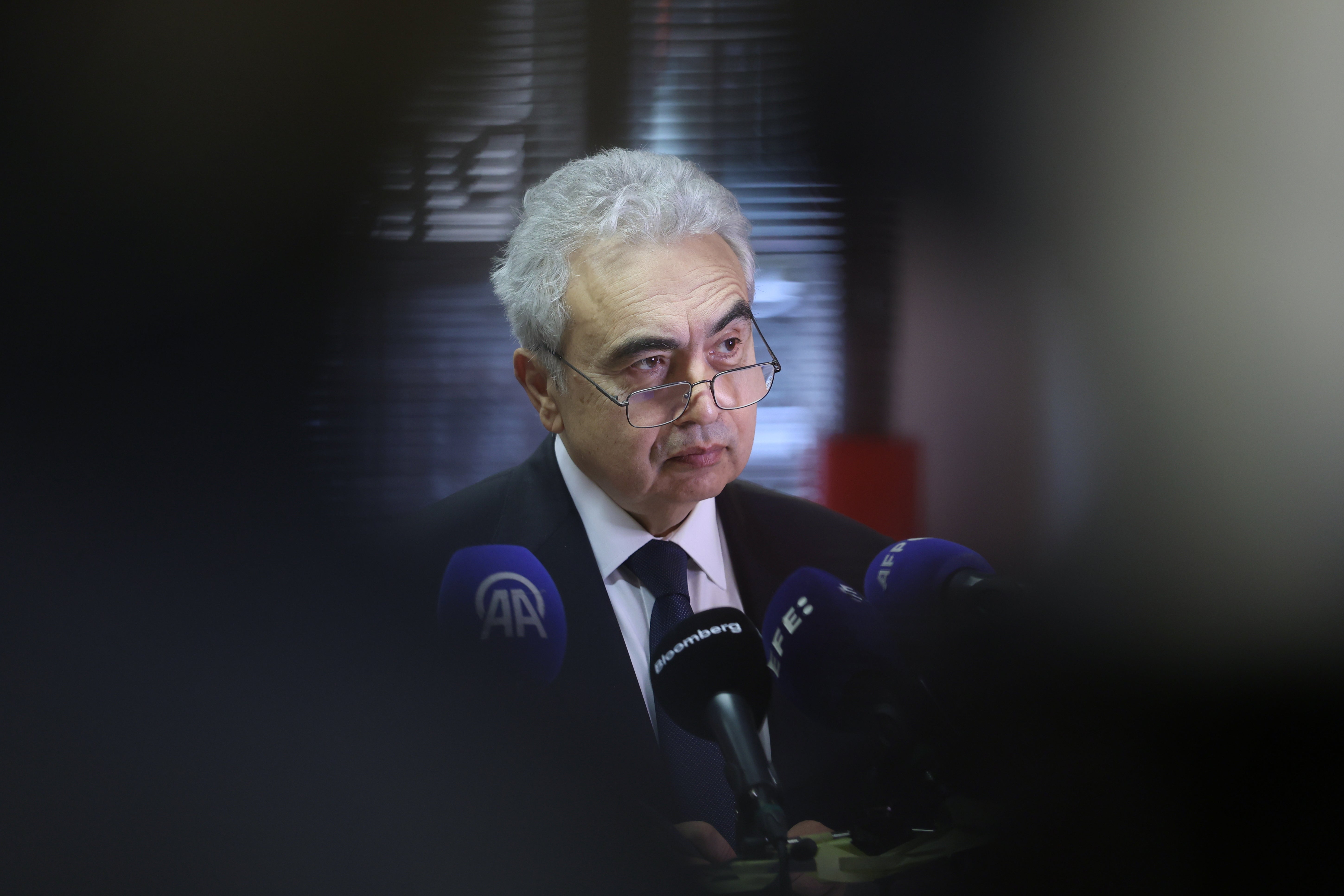 Äldre man med vitt hår och glasögon talar vid mikrofoner under en presskonferens.