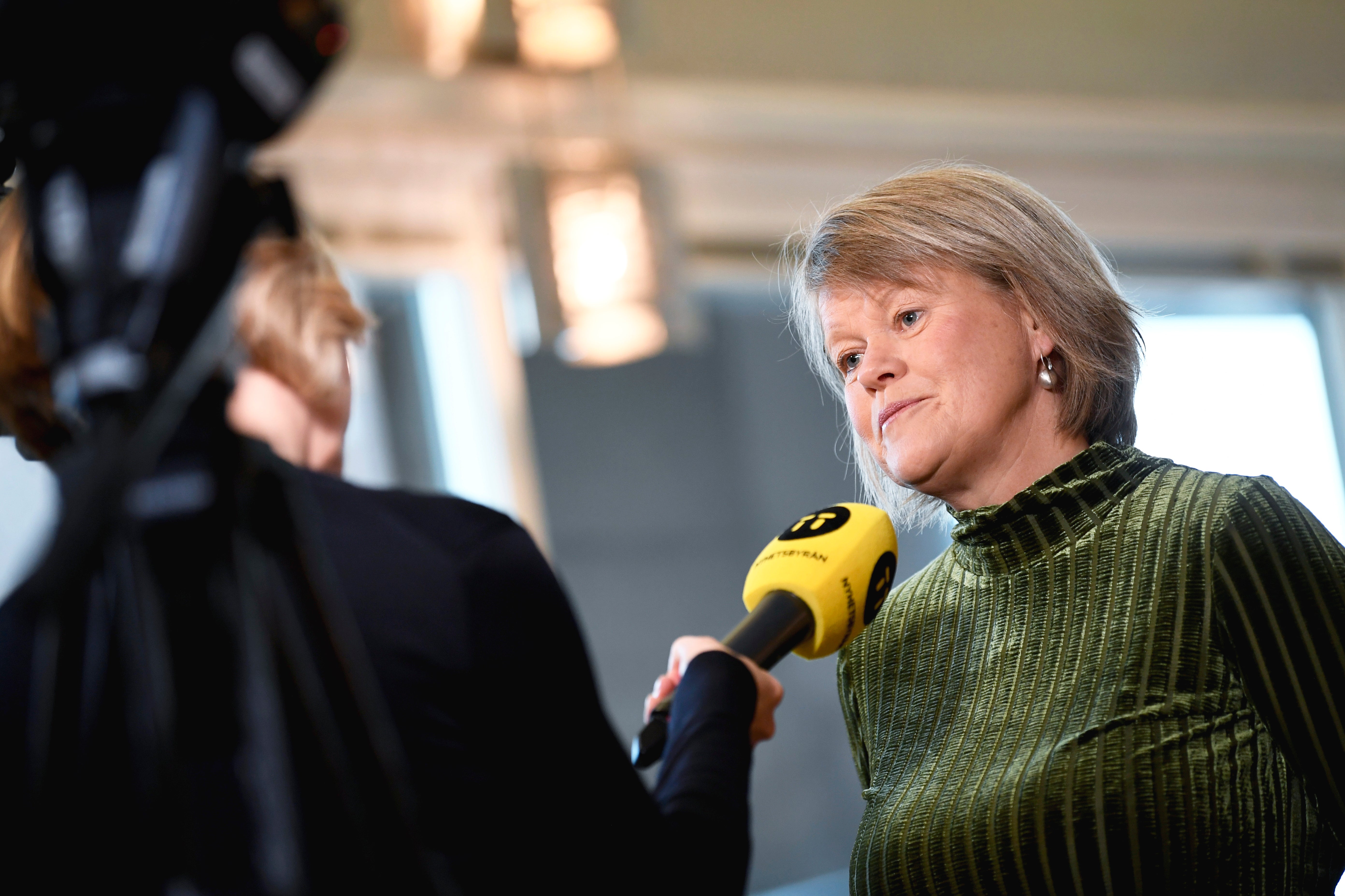 Ulla Andersson intervjuas med en gul mikrofon som hålls fram mot henne.