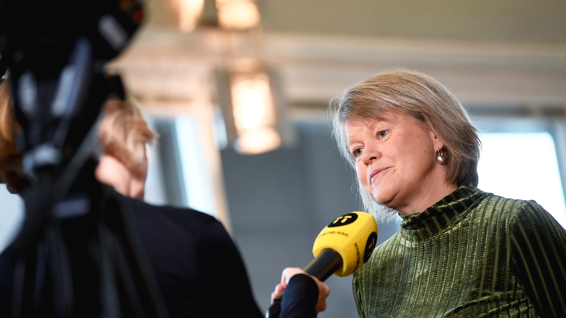 Ulla Andersson intervjuas med en gul mikrofon som hålls fram mot henne.