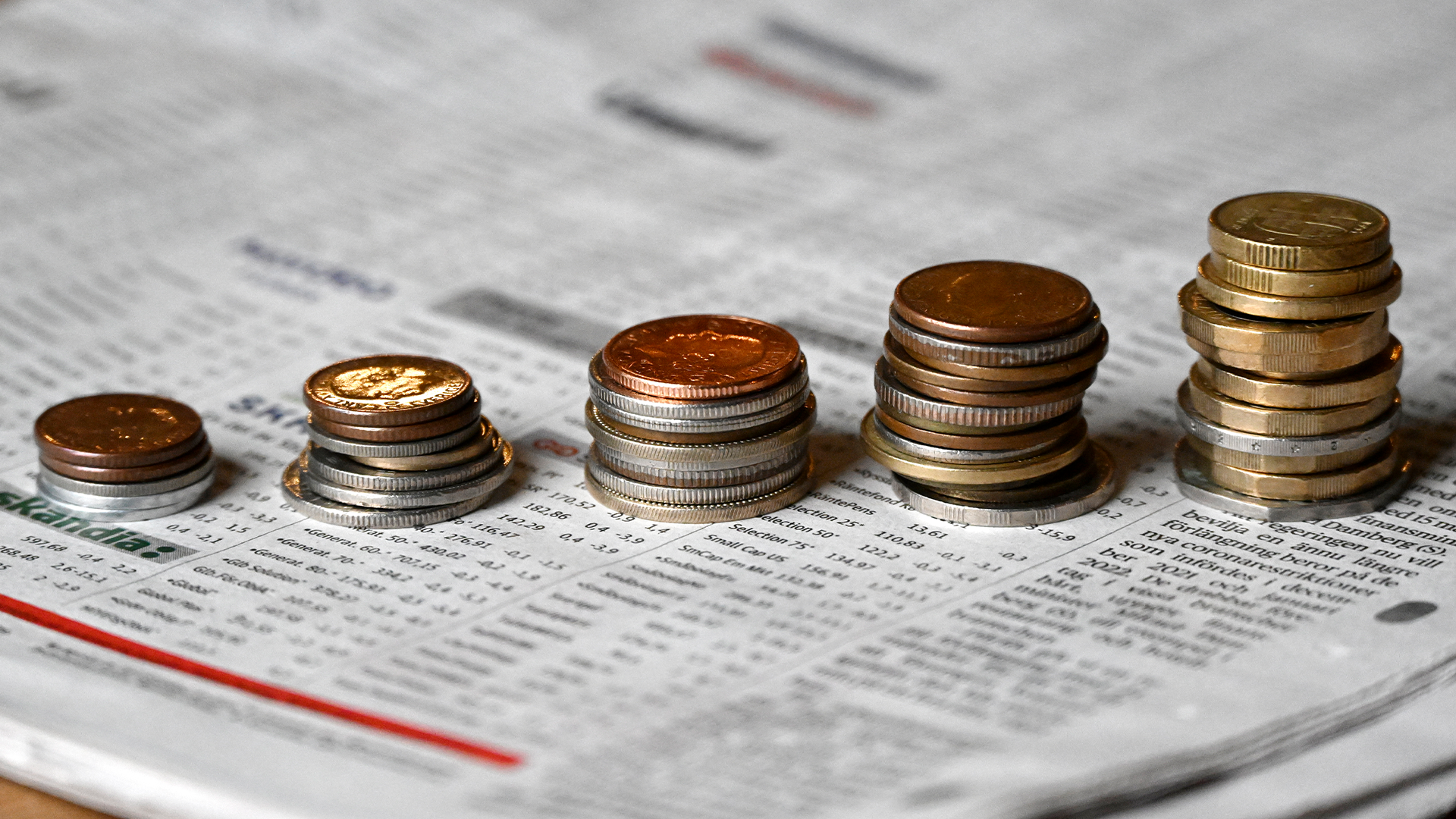 Svenska kronor ligger i olika högar på en papperstidningen med en öppen börssida. 