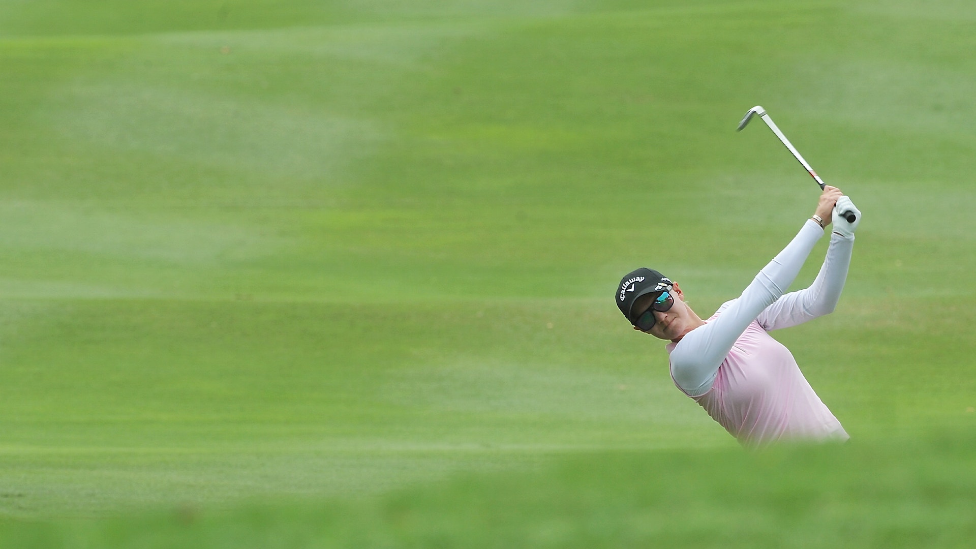 Golfspelare som svingar på en grön golfbana.