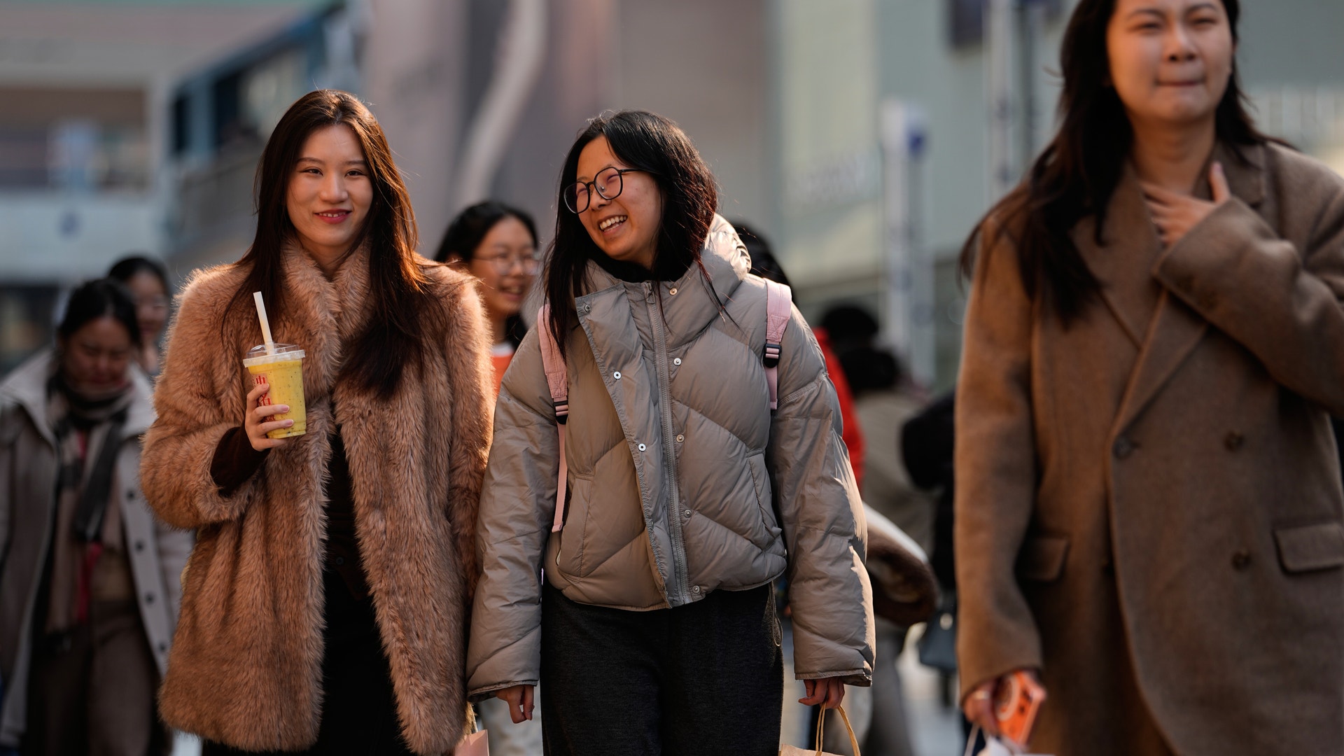 Grupp av unga kvinnor som går tillsammans på en gata i vinterkläder.