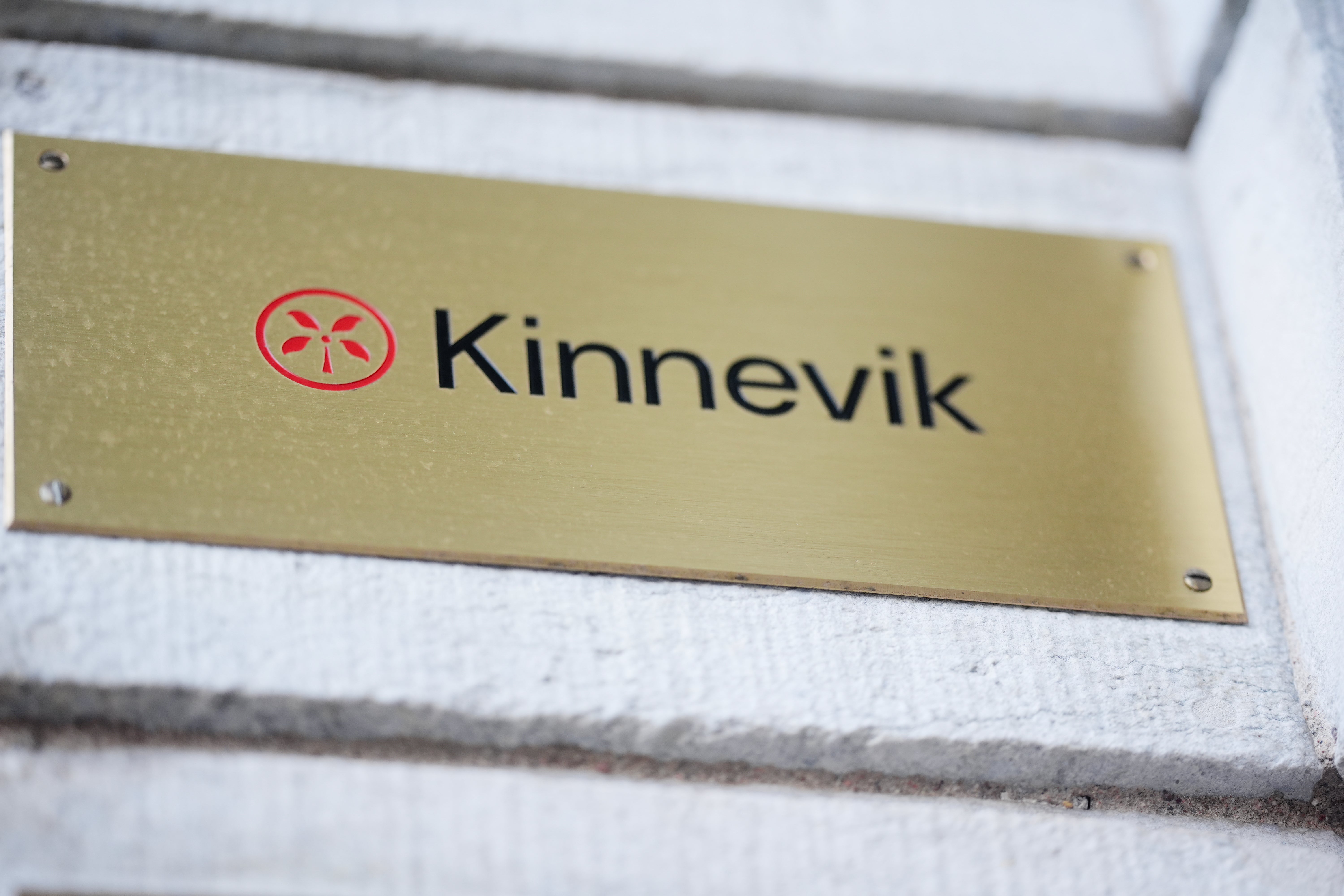 Kinneviks logotyp och namn på en gyllene namnplåt monterad på vit vägg