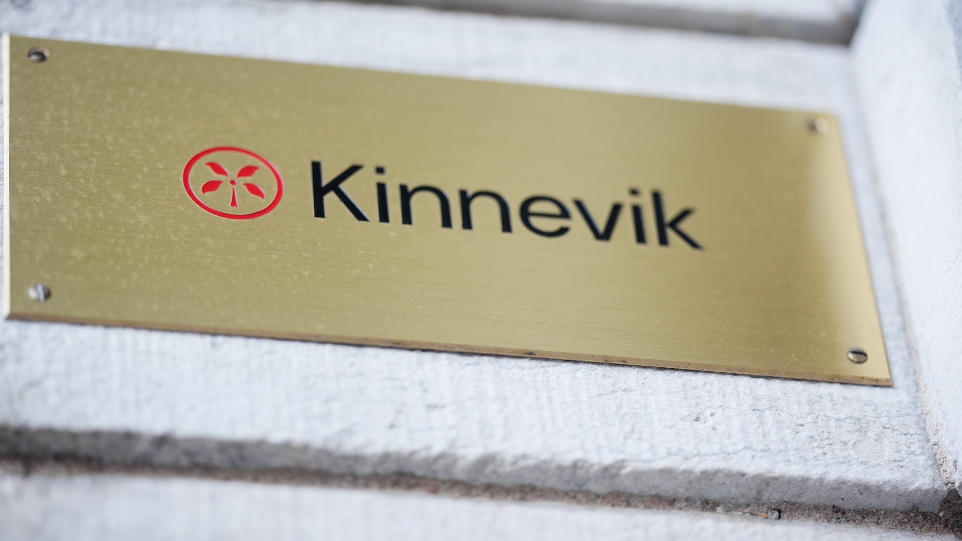 Kinneviks logotyp och namn på en gyllene namnplåt monterad på vit vägg