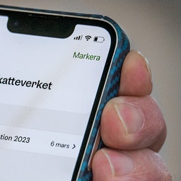 Hand som håller en mobiltelefon med Skatteverkets app öppen på skärmen, som visar inkomstdeklarationen för 2023.