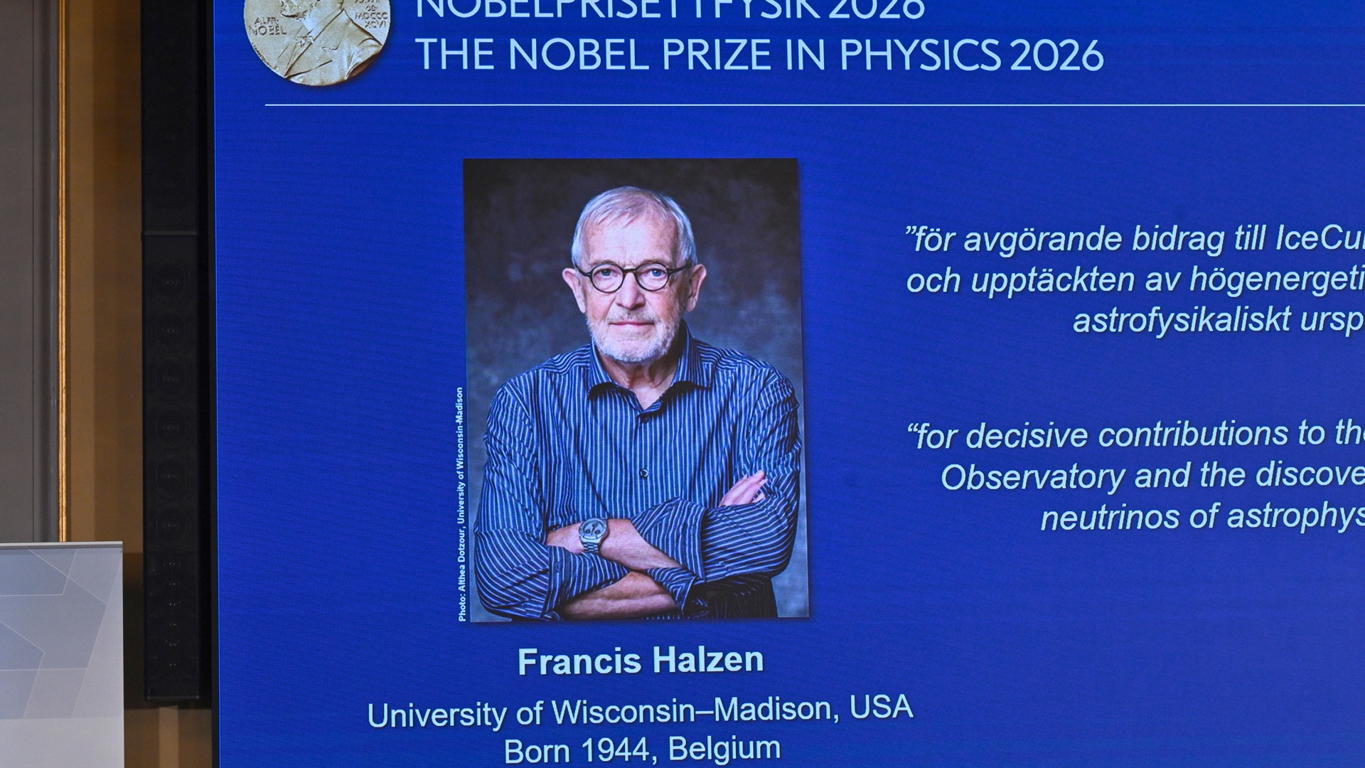 Skärm som visar Nobelpriset i fysik 2026 med ett porträtt av pristagaren Francis Halzen, en äldre man med glasögon och korslagda armar.