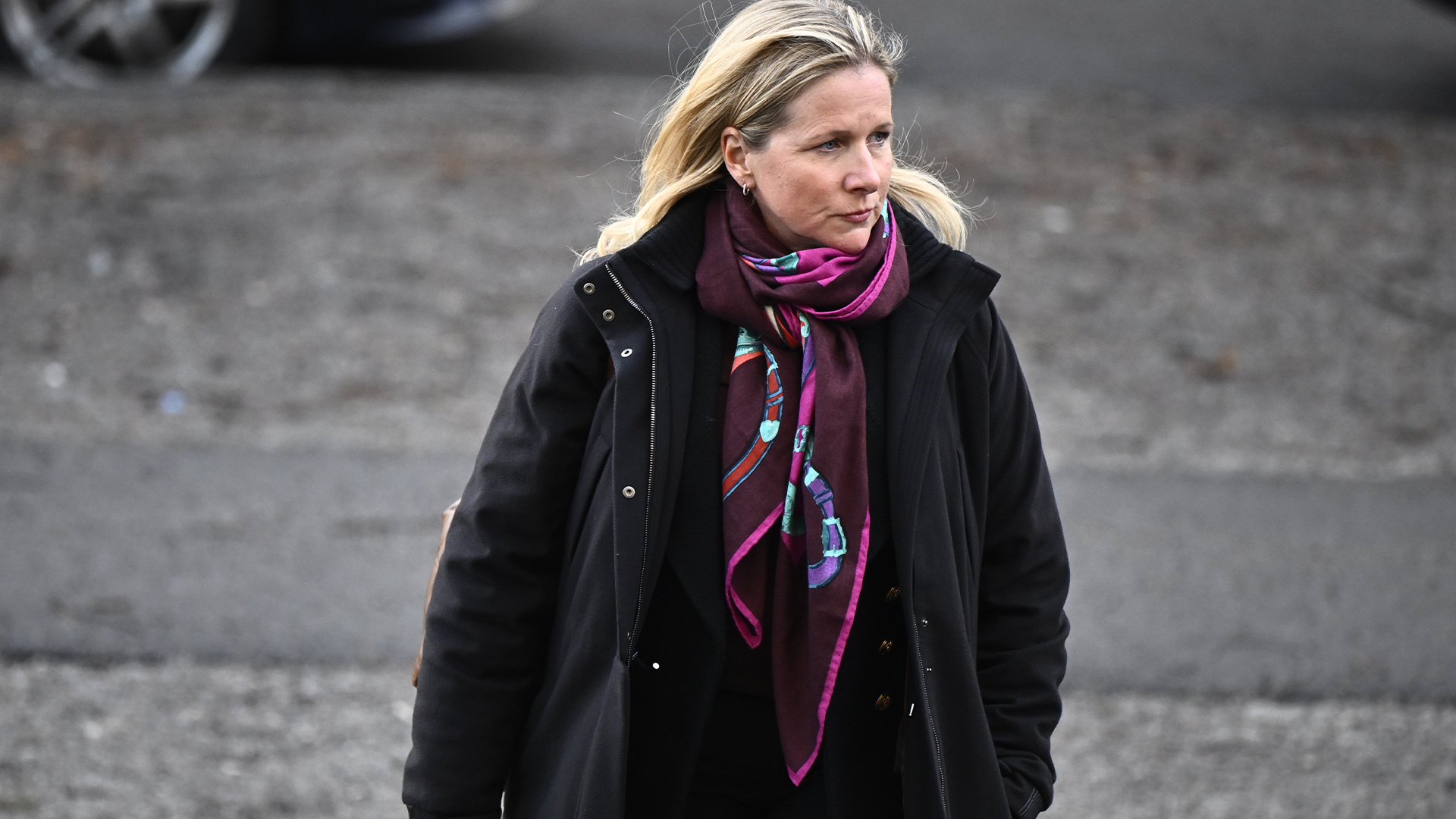 Porträtt av en kvinna med blont hår, svart jacka och lila scarf