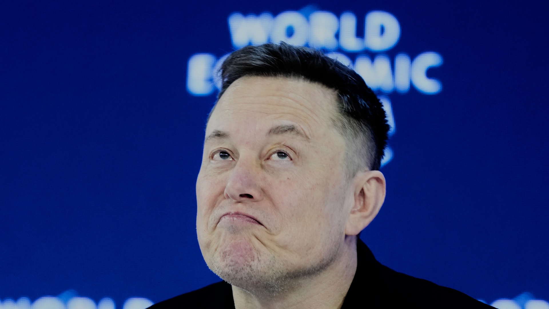 Porträttfoto av en man i svart skjorta framför en blå bakgrund med World Economic Forum-logotyp