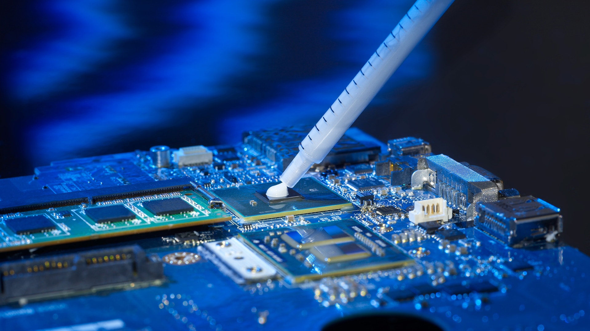 Närbild av ett elektroniskt kretskort med blå belysning där en vit testspets inspekterar de små komponenterna och ledarna på kortet.