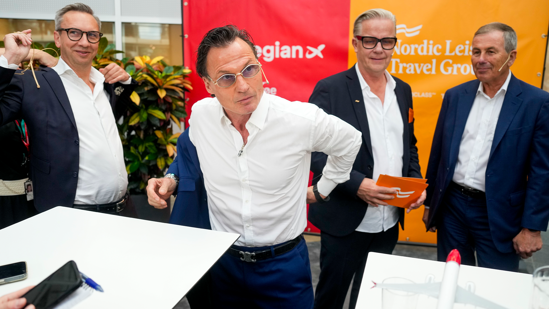 Fyra män i affärskläder står tillsammans framför en bakgrund med företagslogotyper.