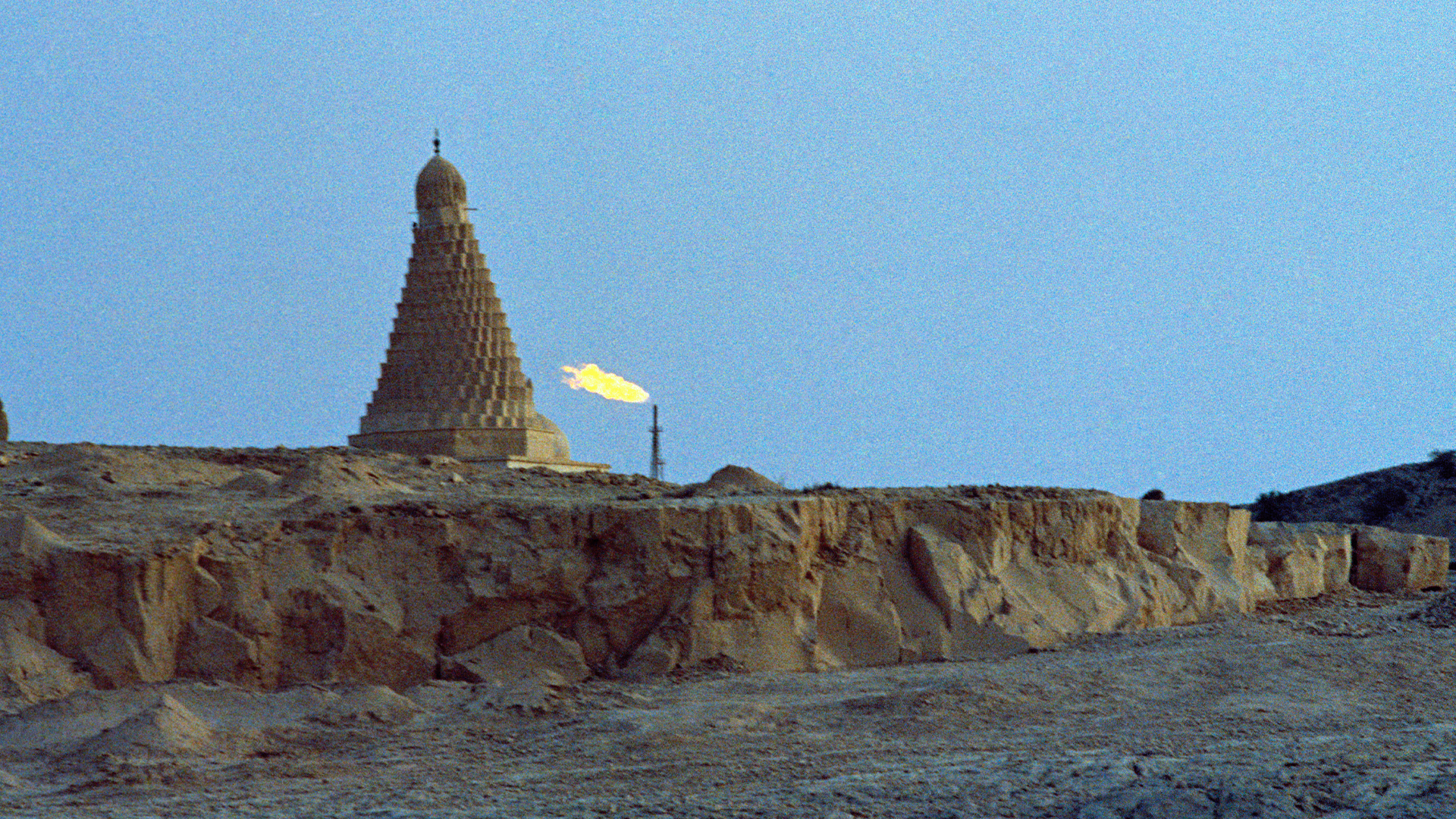 Pyramidformad struktur på öken med gul flagga mot blå himmel