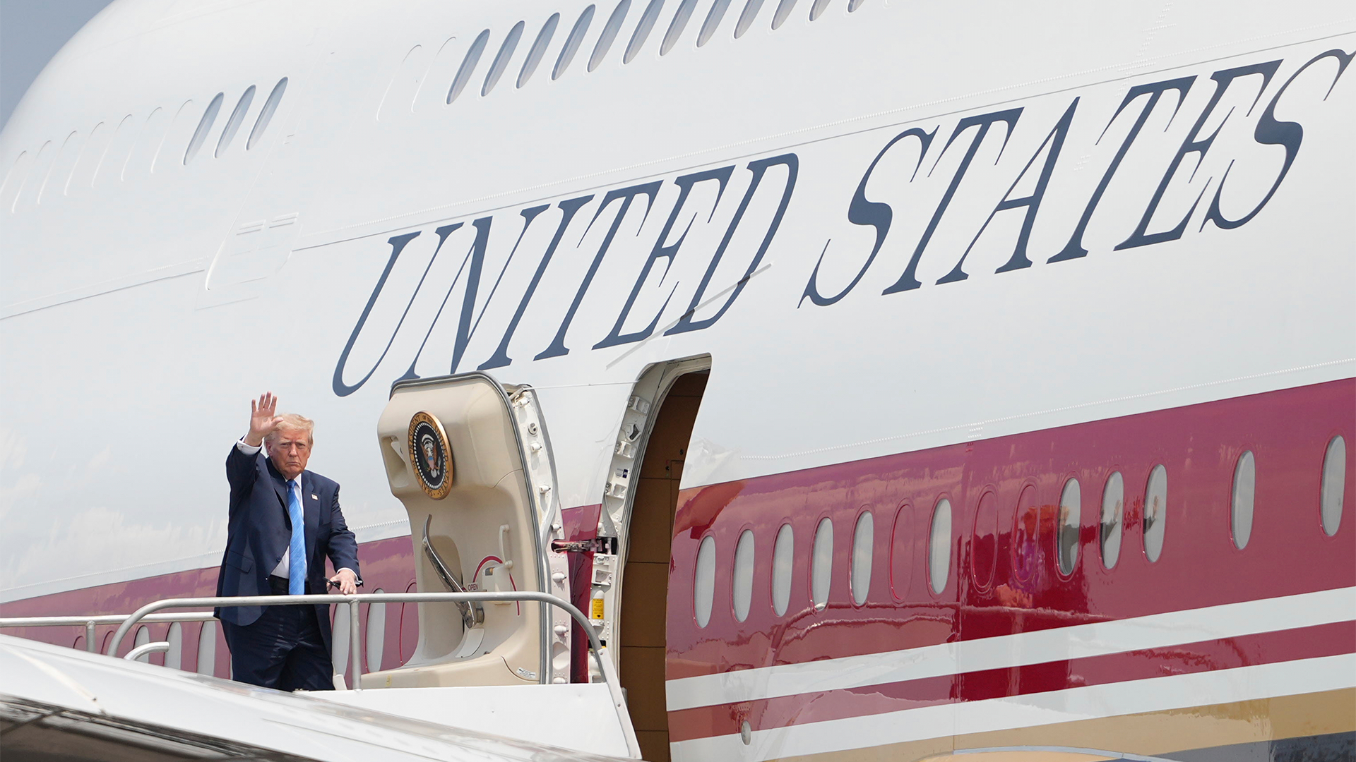 Man i kostym viftar från trappan vid ett amerikanskt regeringsflygplan.