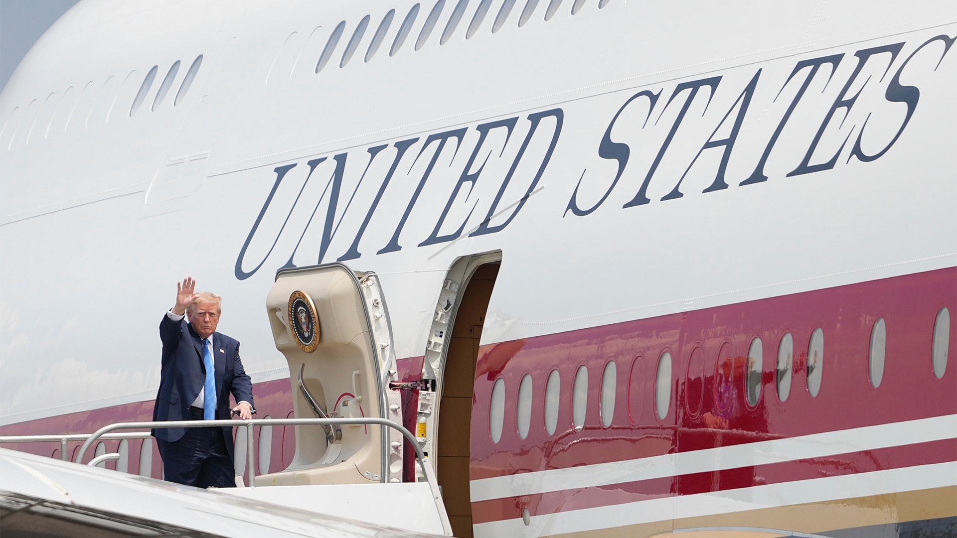 Man i kostym viftar från trappan vid ett amerikanskt regeringsflygplan.