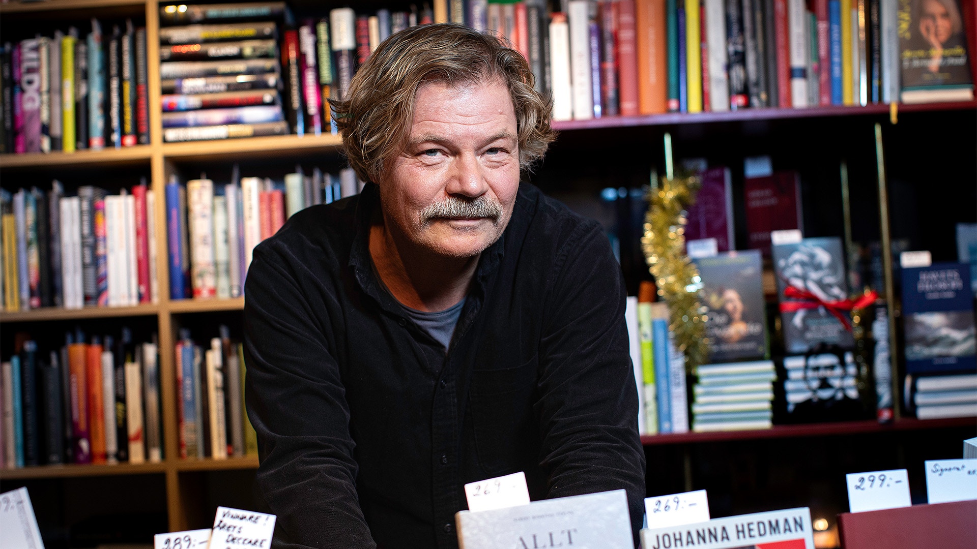 En man med glasögon och rutigt jackett talar vid en mikrofon under en formell tillställning.