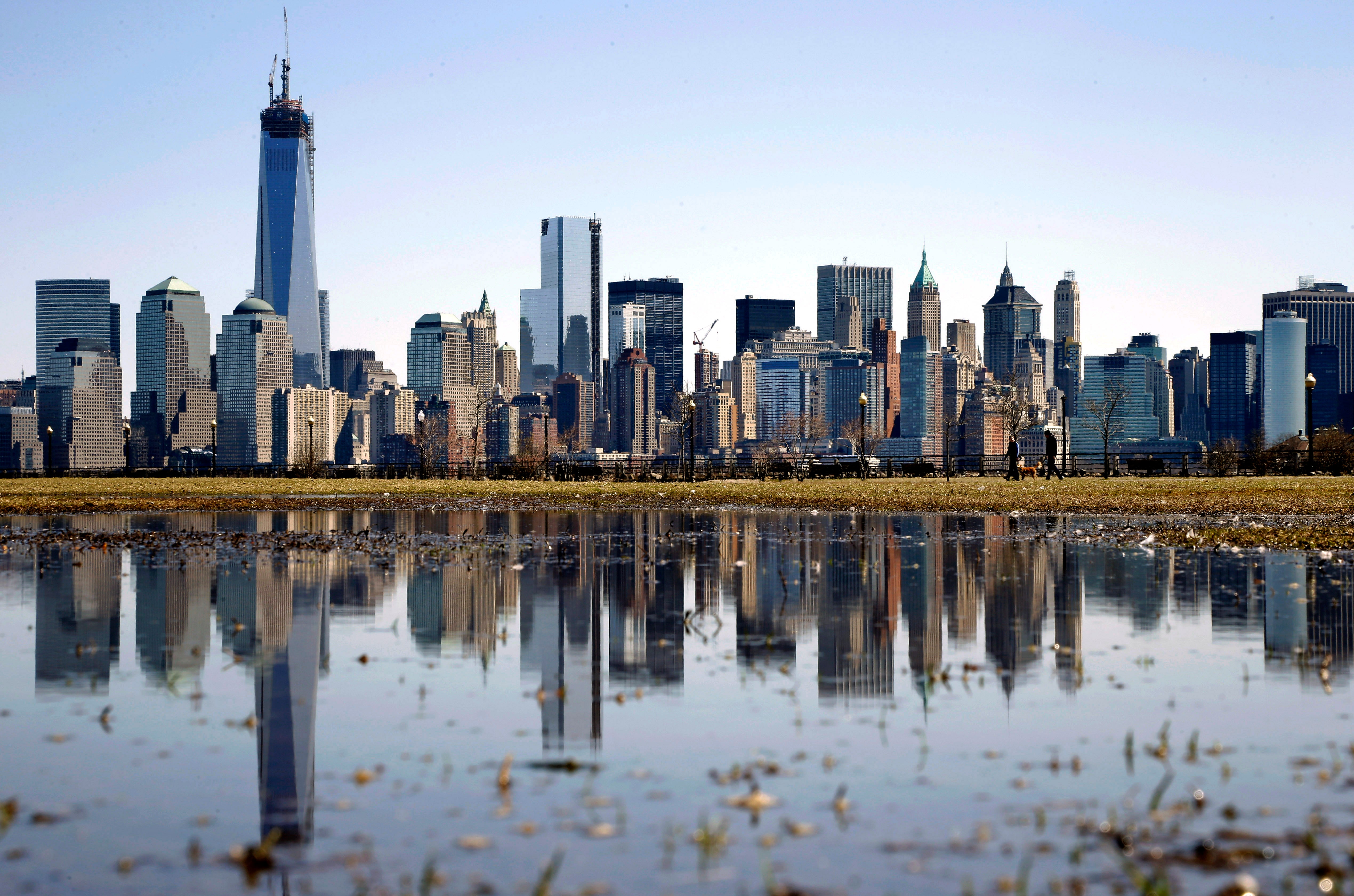 Skyline över Manhattan i New York med höga skyskrapor som speglas i en vattenpöl i förgrunden.