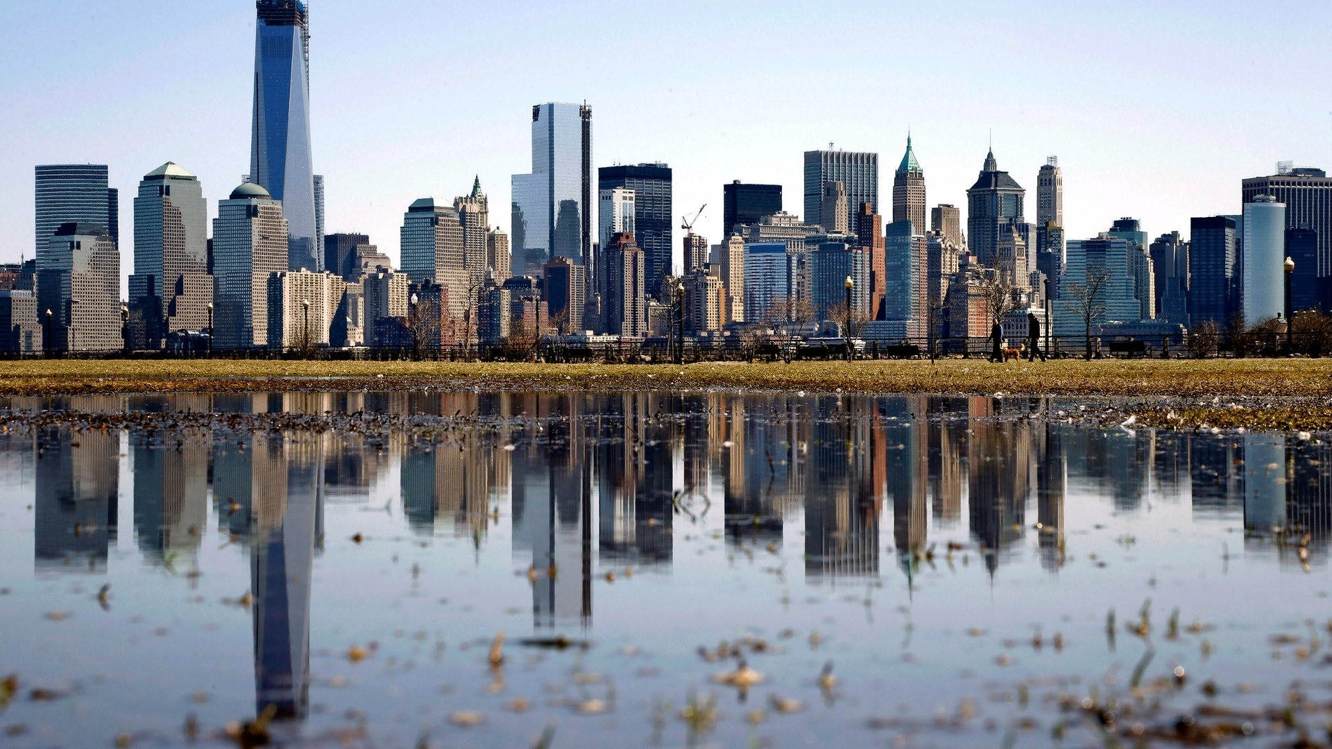 Skyline över Manhattan i New York med höga skyskrapor som speglas i en vattenpöl i förgrunden.