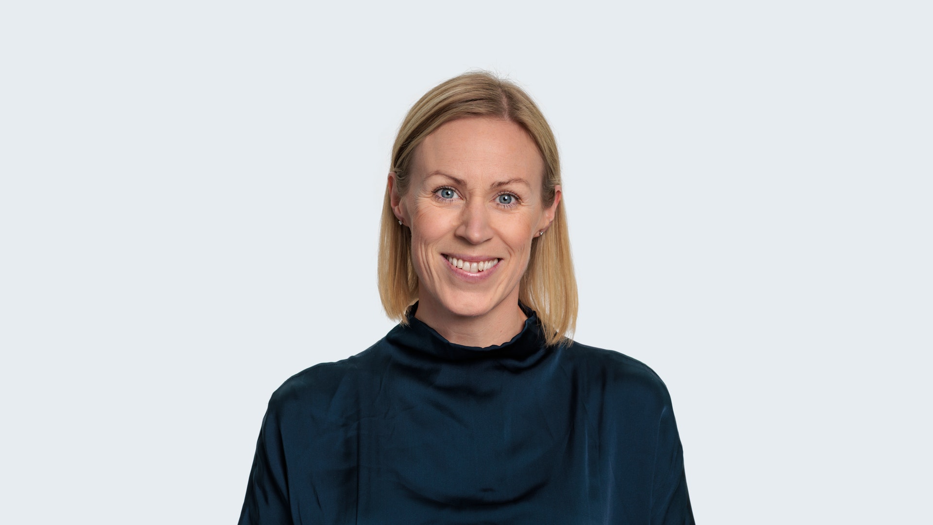 Porträtt av en leende kvinna med axellångt blont hår, klädd i en mörkblå blus, mot en ljus bakgrund.