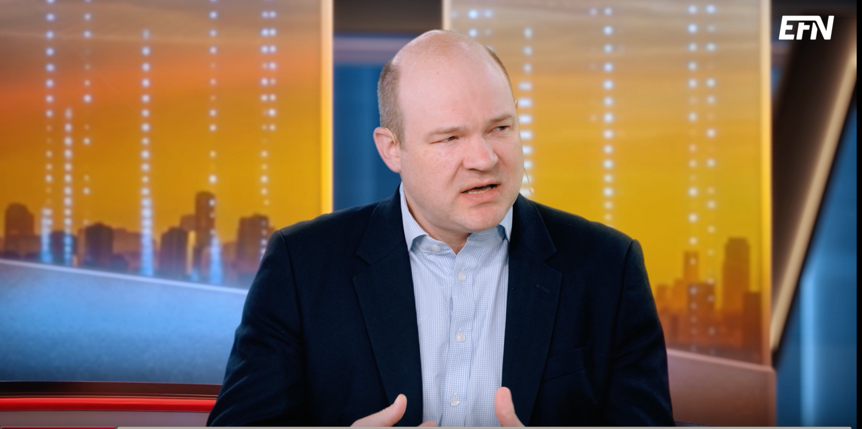 En man i kostym pratar och gestikulerar med händerna i en tv-studio.