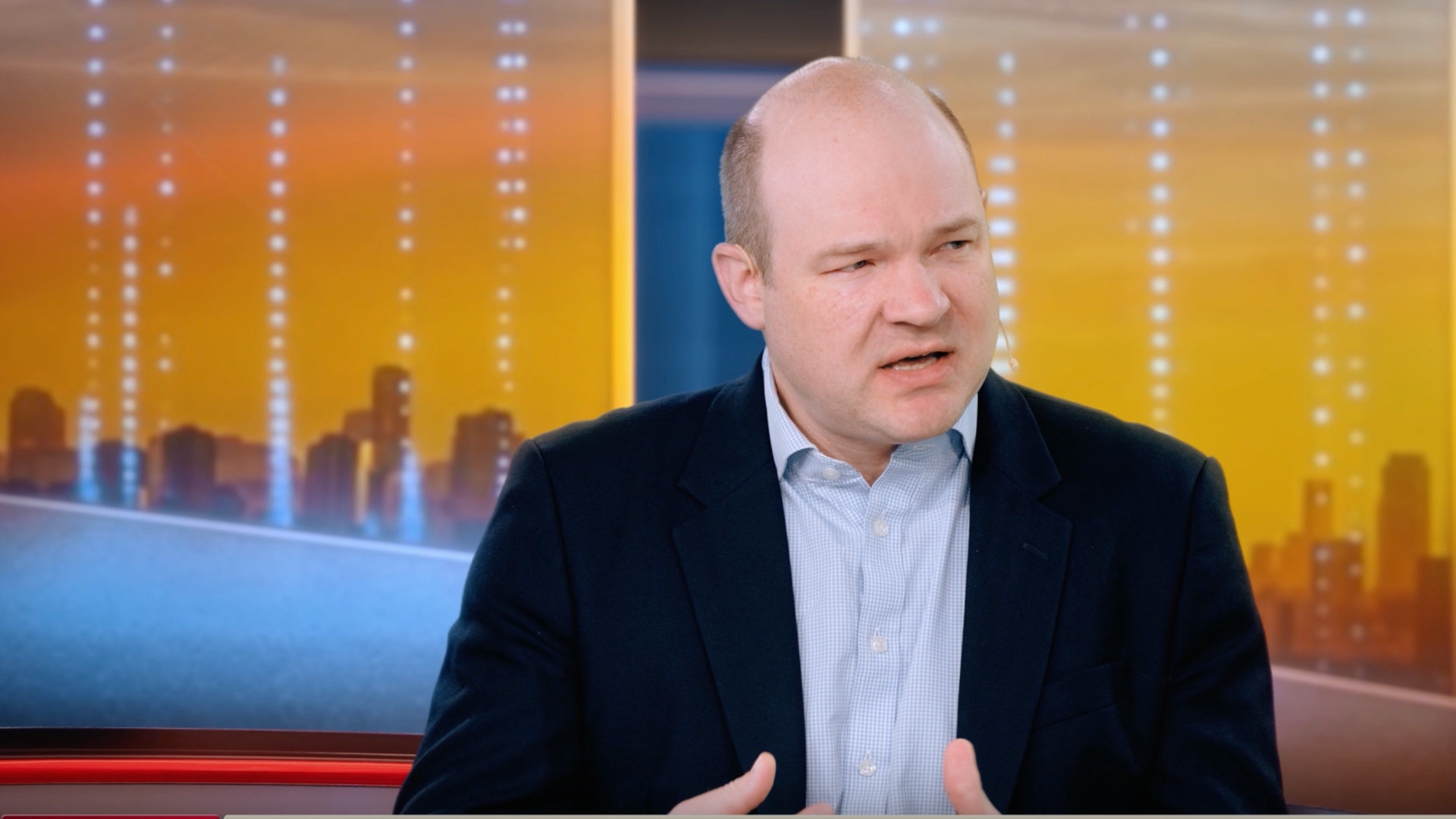 En man i kostym pratar och gestikulerar med händerna i en tv-studio.