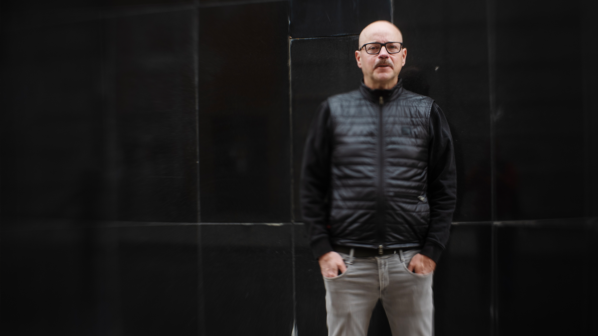 Pål Ahlsén står vid en svart vägg. Han har svart väst och tjocktröja på sig.