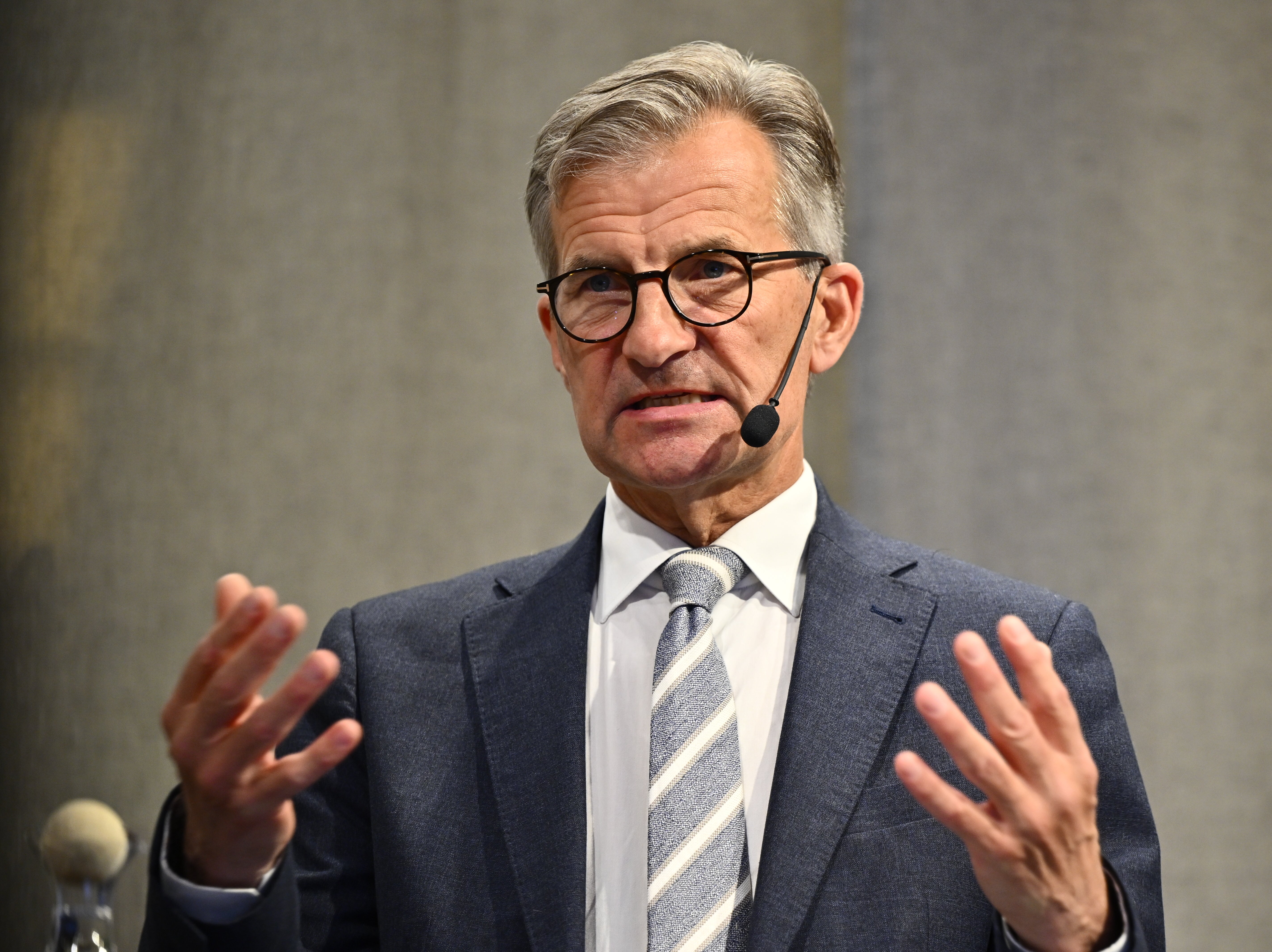 Man i kostym och glasögon håller ett föredrag med headset-mikrofon och gestikulerar med händerna.