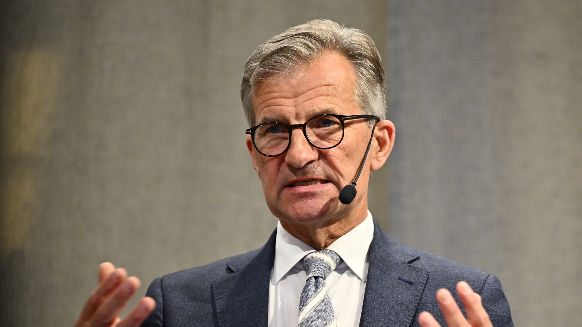 Man i kostym och glasögon håller ett föredrag med headset-mikrofon och gestikulerar med händerna.