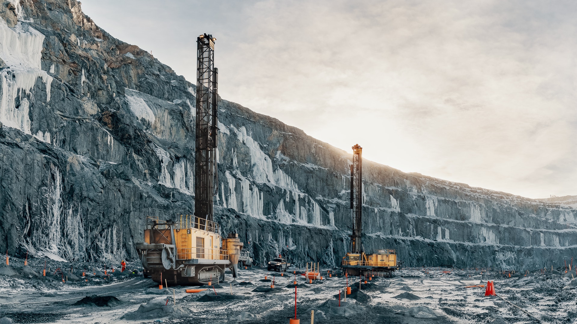 Gul borrningsmaskin vid en stor öppen gruvgrop med höga bergväggar.