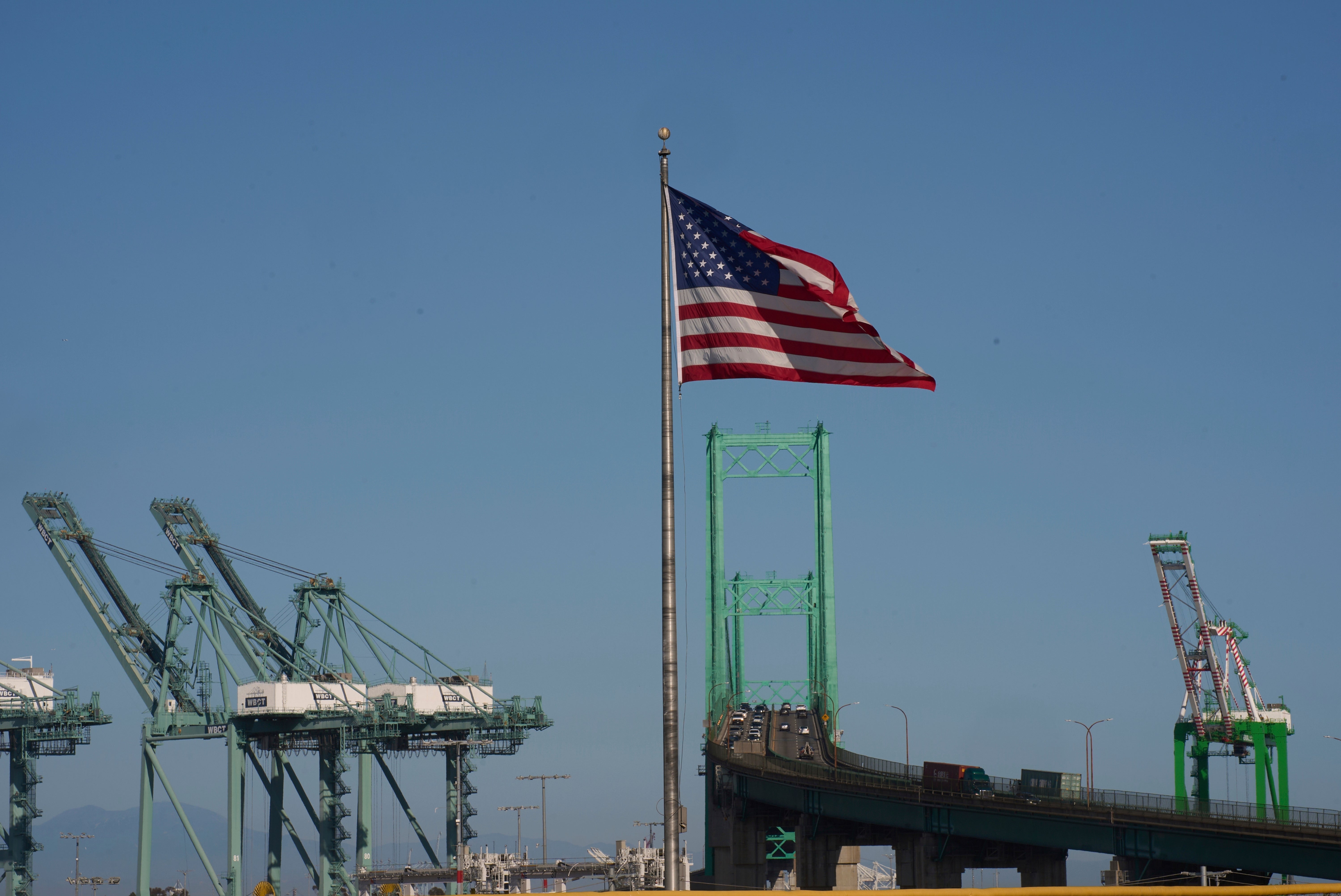 Amerikansk flagga som vajar på en flaggstång vid en containerhamn med lastningsekipage i bakgrunden