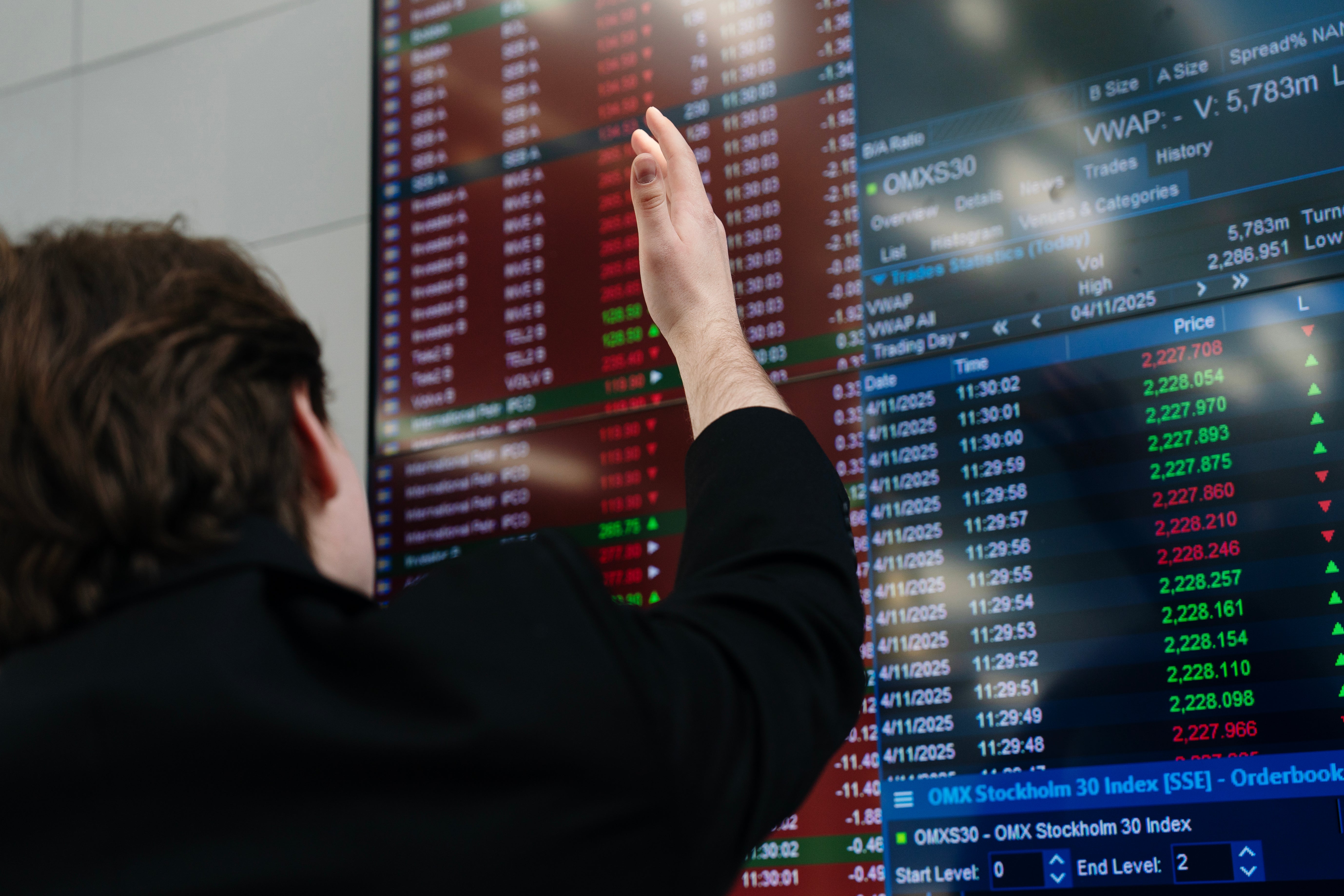 En person pekar på en aktiemarknadsskärm med finansiell data och börskurser.