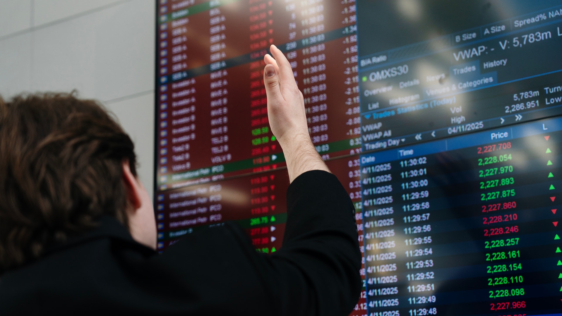 En person pekar på en aktiemarknadsskärm med finansiell data och börskurser.