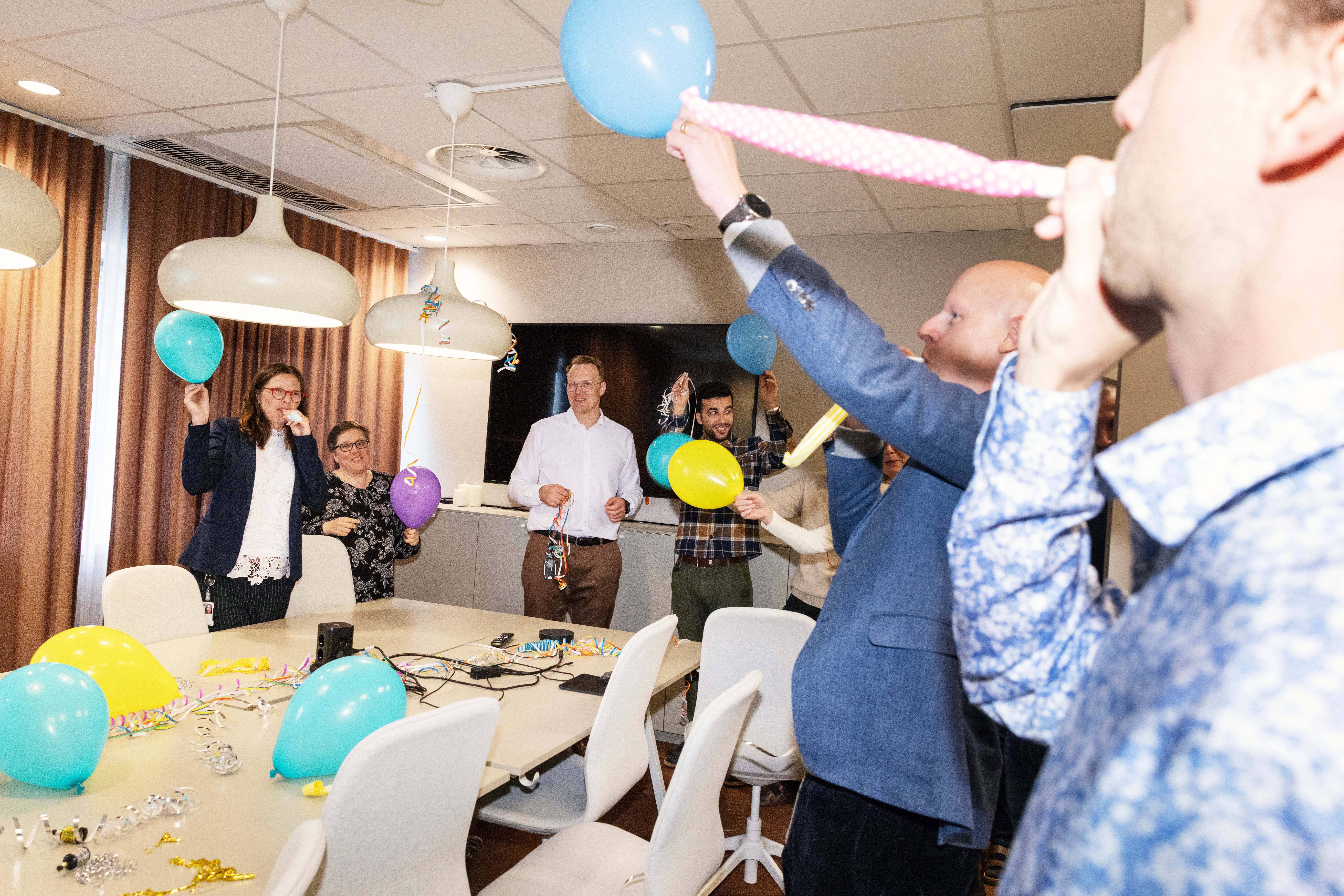 Kollegor firar tillsammans i ett konferensrum med ballonger och konfetti på bordet.